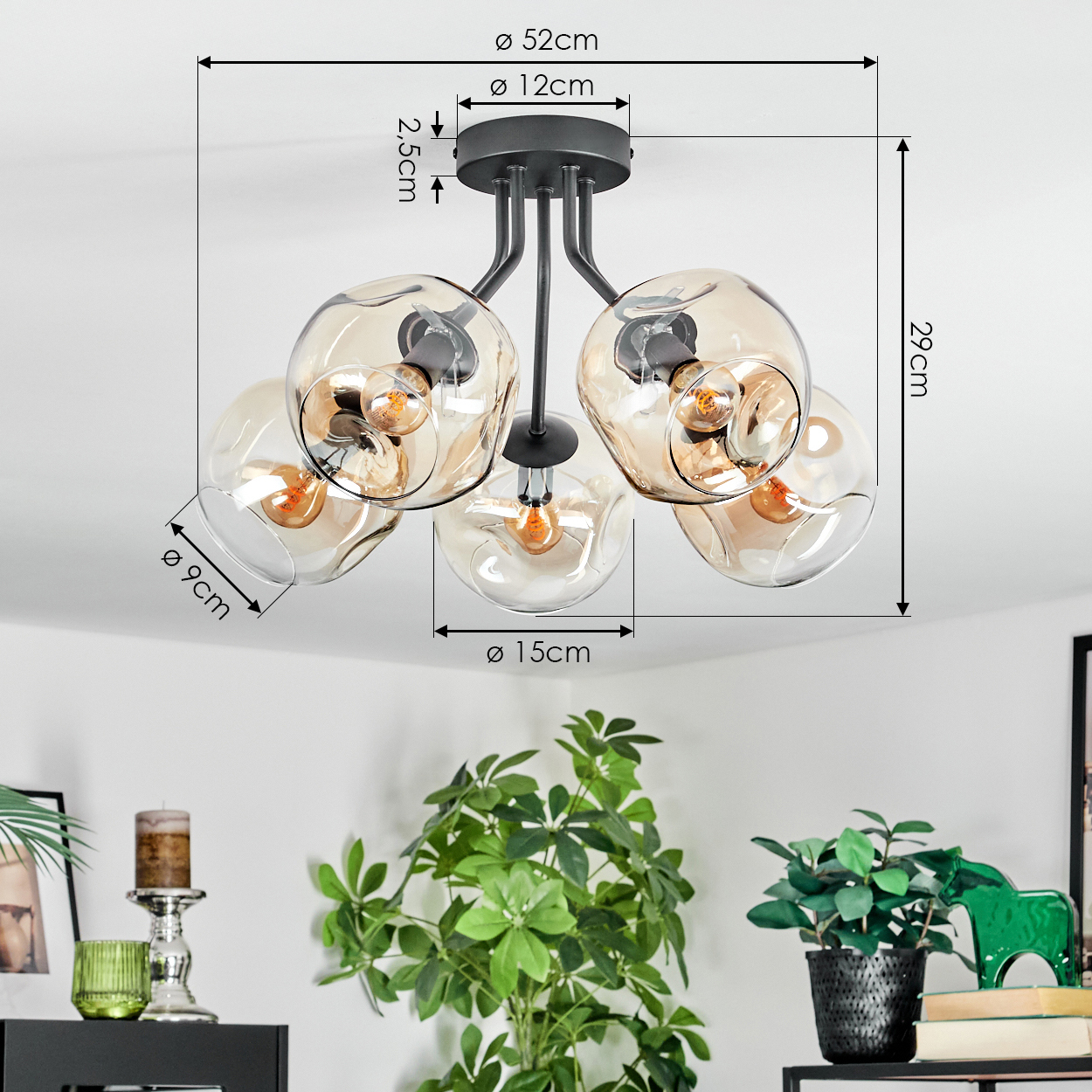 Moderne Deckenlampe mit fünf Glaskugeln, Maße angegeben. Darunter Pflanzen und Dekorationsartikel auf schwarzer Oberfläche.