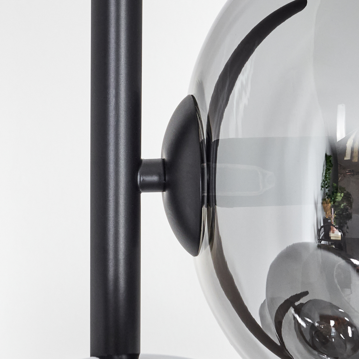 Nahaufnahme einer Lampe mit schwarzem Metallpfosten und transparentem, rauchigem Glasschirm. Der Hintergrund ist weiß.