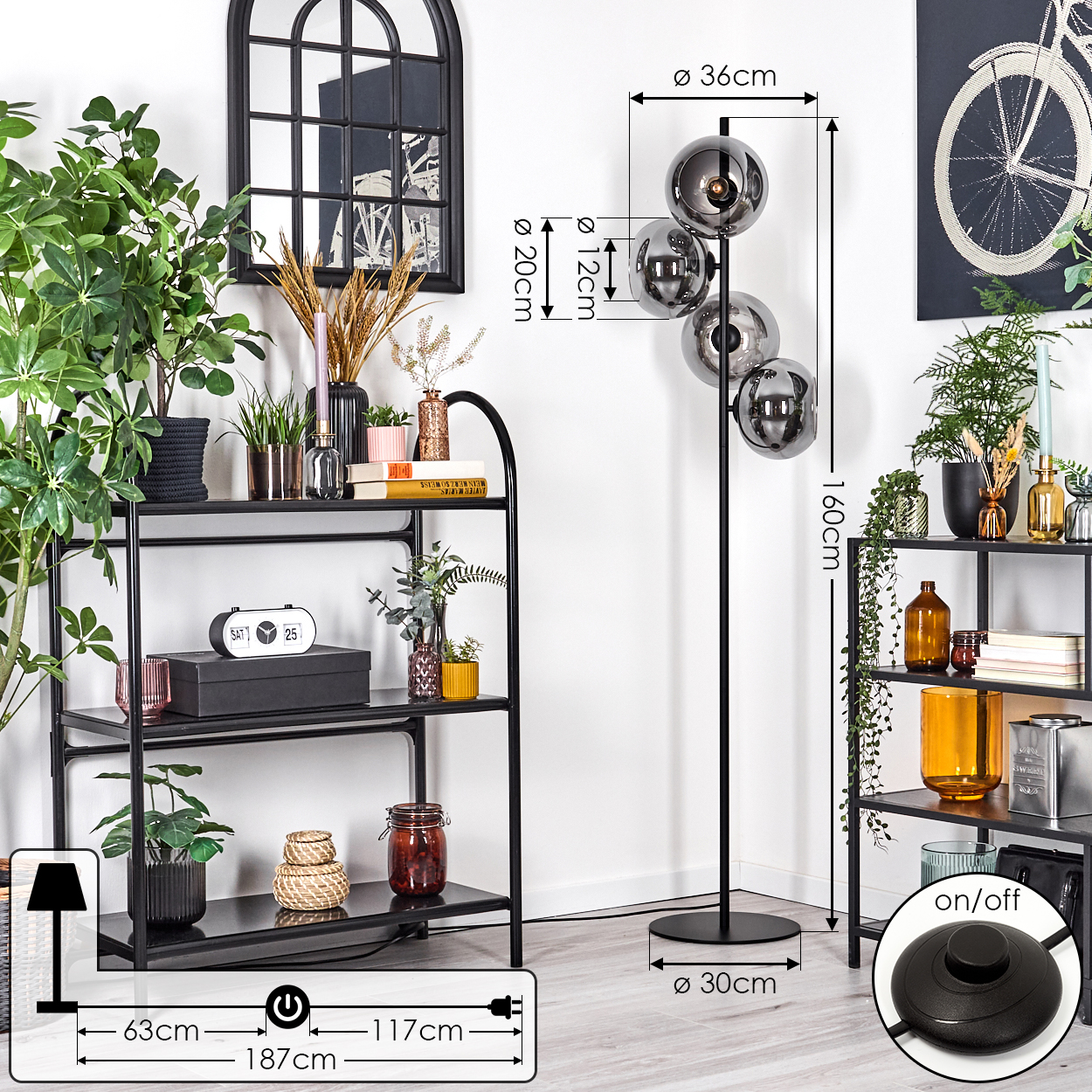 Ein modernes Wohnzimmer mit einer schwarzen Stehlampe mit Glaskugeln. Regale mit Pflanzen, Spiegel und ein Gemälde sind sichtbar.
