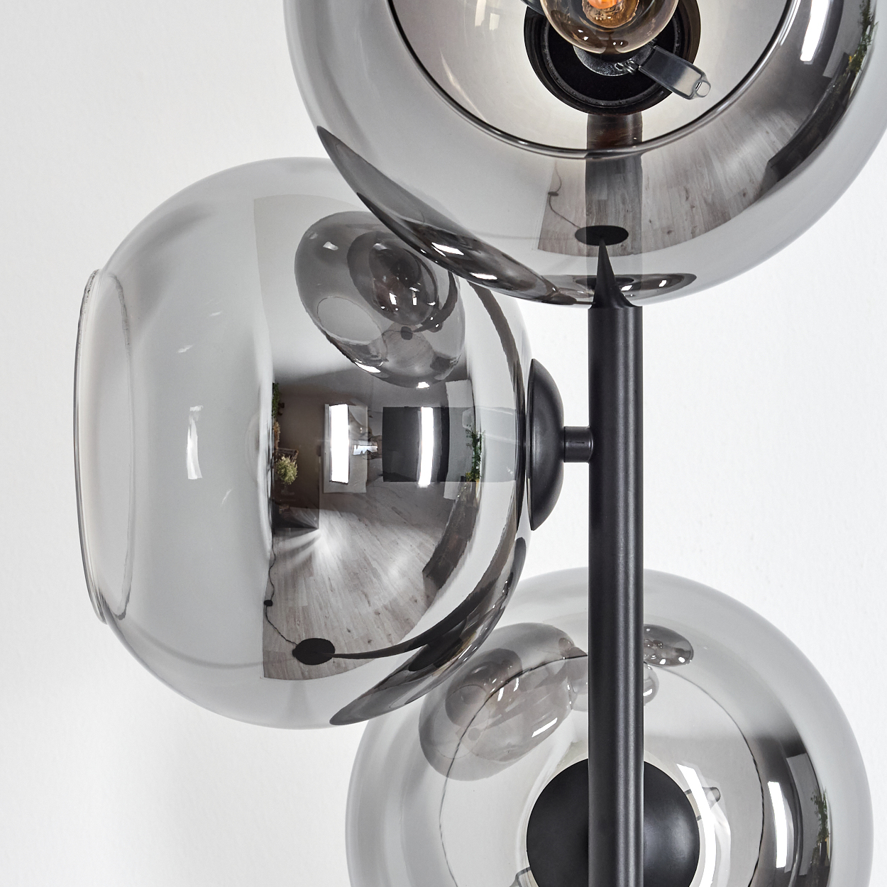Eine moderne Lampe mit drei grauen Glaskugeln. Die Kugeln reflektieren den Raum. Die Lampe hat ein schwarzes Metallgestell. Weißer Wandhintergrund.