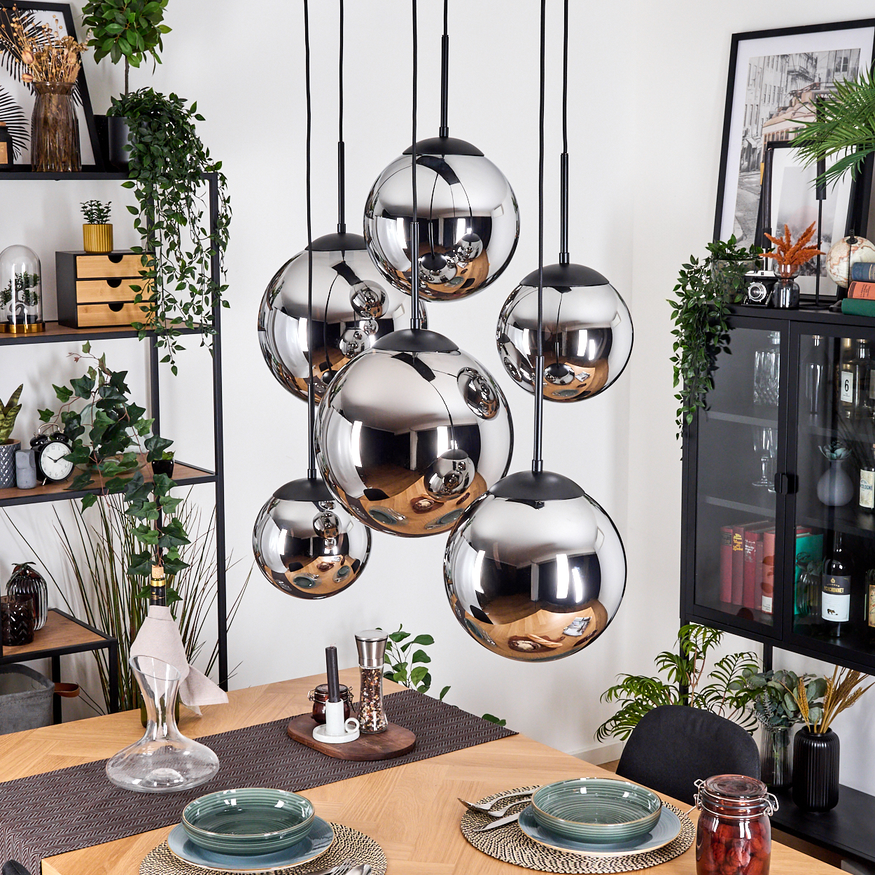 Chrom-Kugel-Pendelleuchten über einem Holzesstisch, der für eine Mahlzeit gedeckt ist. Regale und Schrank im Hintergrund.