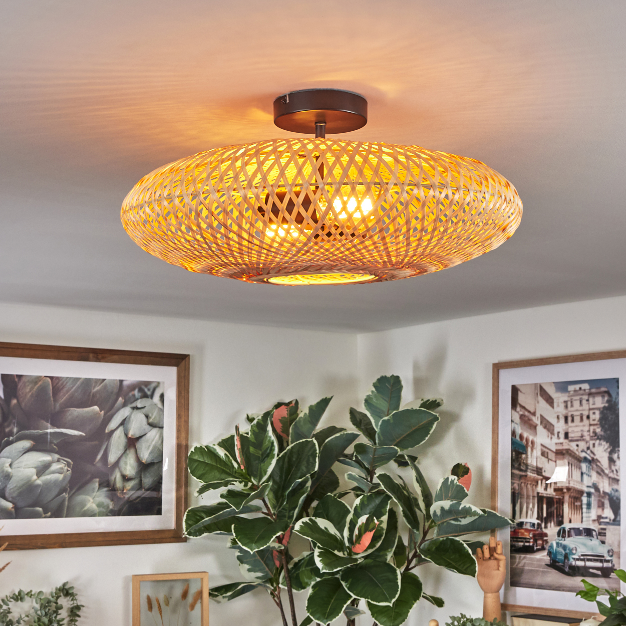 Eine gewebte, hellbraune Deckenlampe beleuchtet einen Raum. Darunter dekorieren Pflanzen und gerahmte Bilder den Raum.
