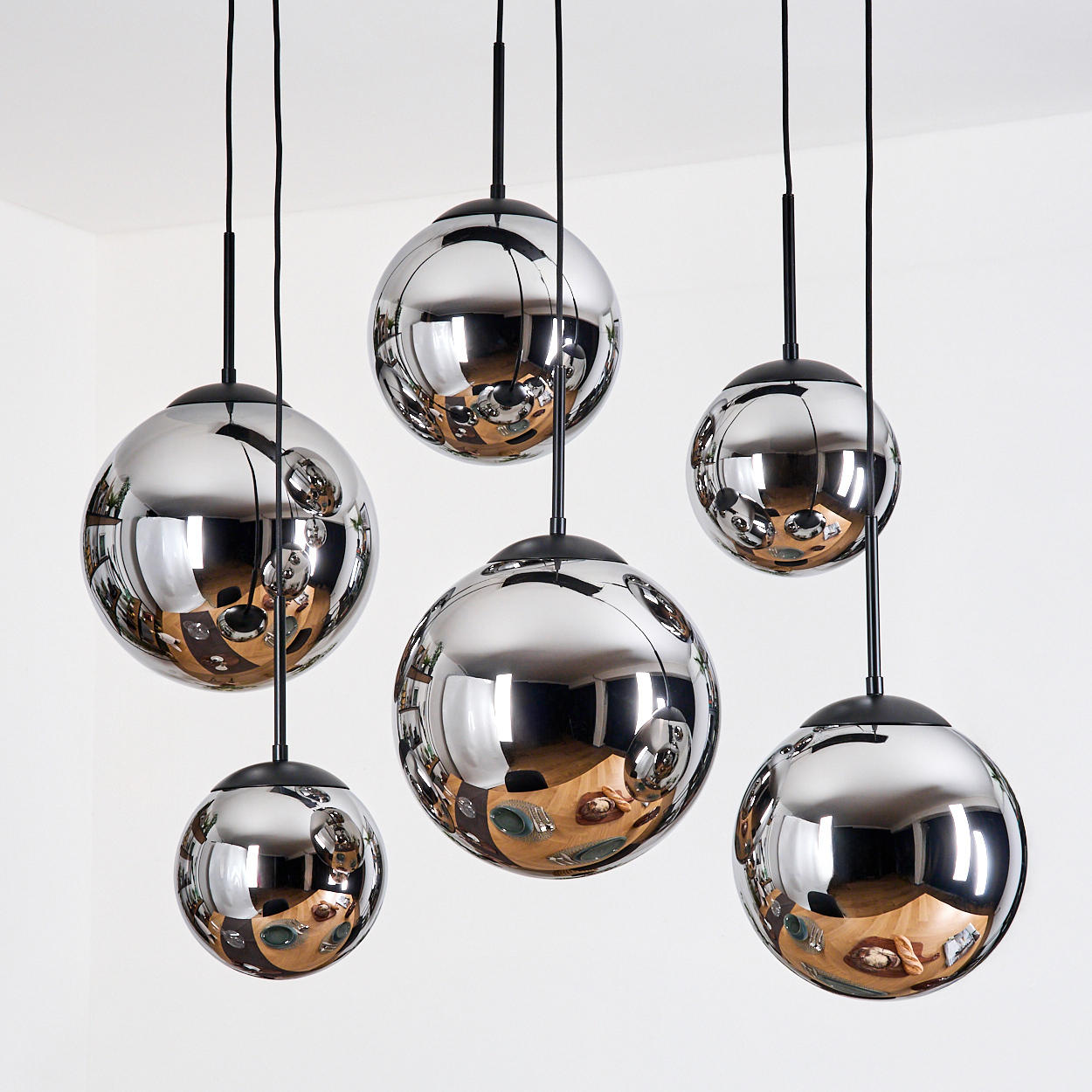 Sechs verchromte Kugel-Pendelleuchten reflektieren einen Raum mit einem Holztisch, Tellern und Essen, der von einer weißen Decke abgehängt ist.