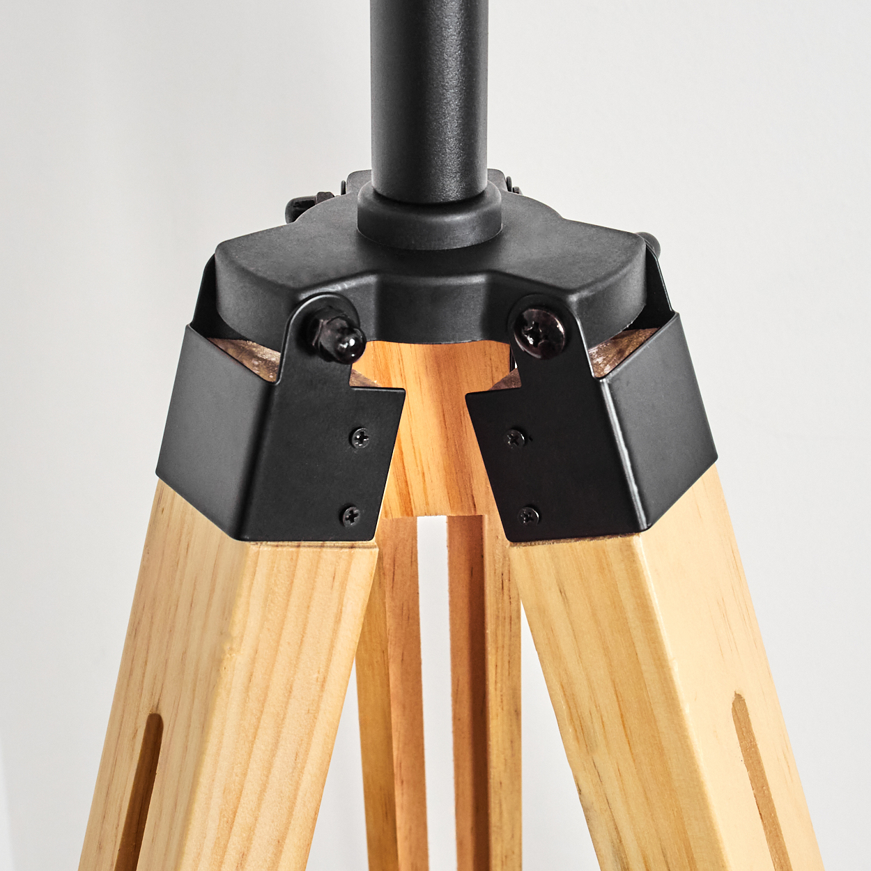 Nahaufnahme eines hölzernen Stativ-Lampenfußes. Schwarze Metallakzente und Schrauben sichern die Beine. Helle Holzbeine bilden eine stabile Basis.