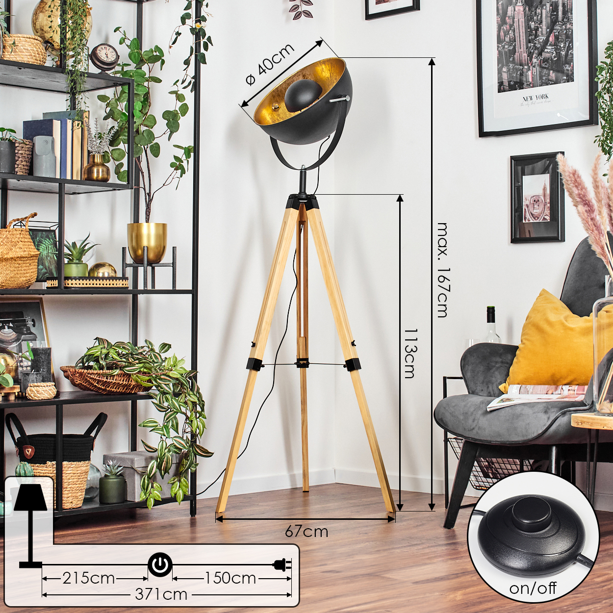Eine schwarz-goldene Stehlampe mit Holzbeinen steht in einem Raum. Links ein Regal mit Deko. Rechts ein Stuhl und Kunstwerk.