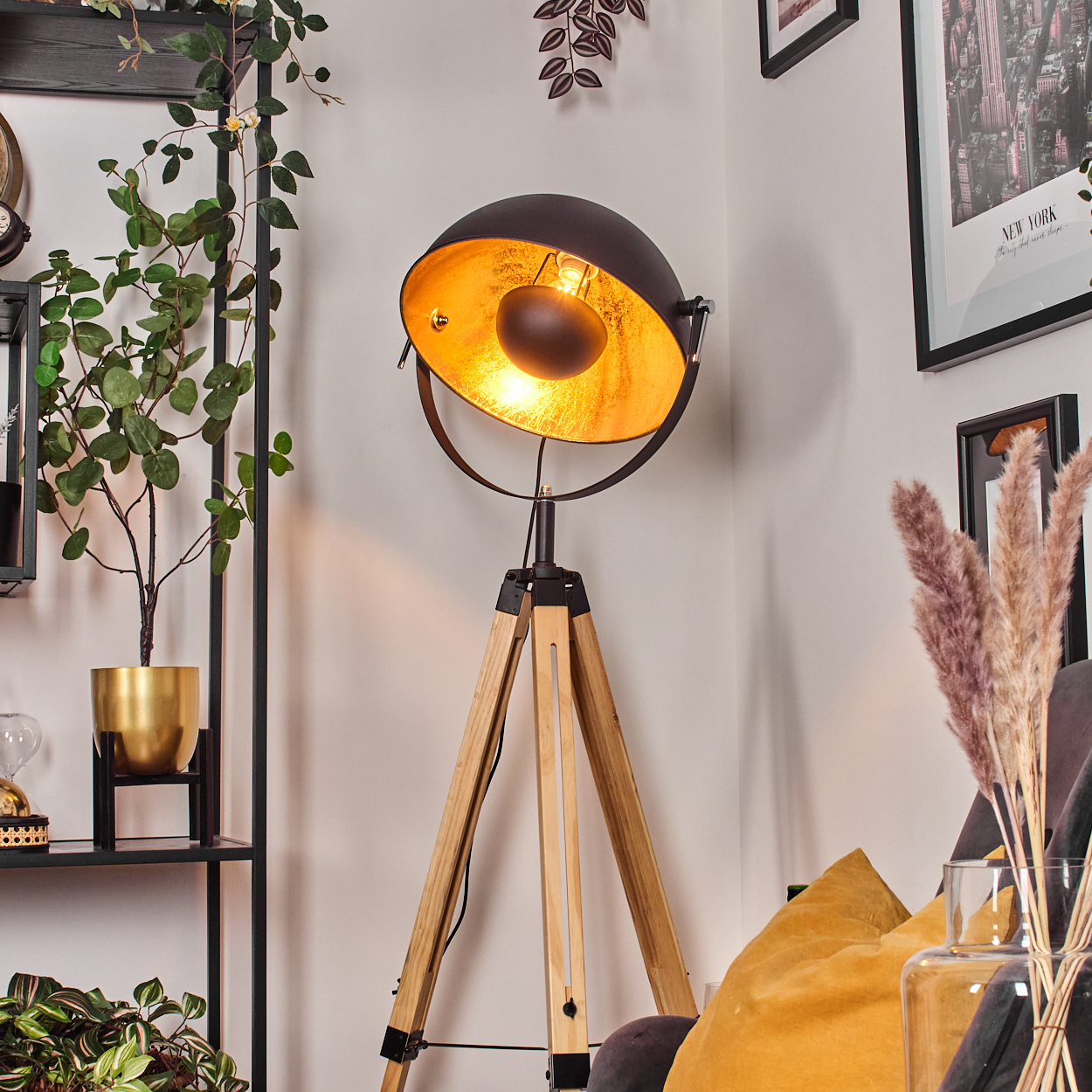 Eine moderne Stehlampe mit schwarzem Schirm und goldener Innenausstattung steht auf Holzbeinen. Pflanzen, gerahmte Kunst und Kissen vervollständigen die Szene.
