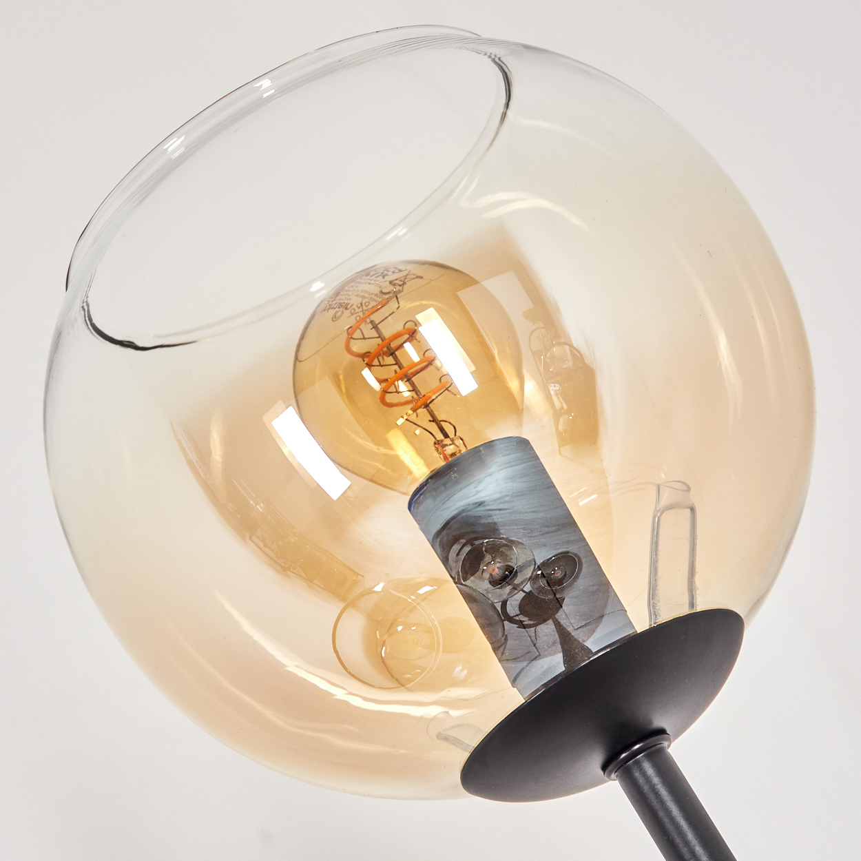 Nahaufnahme einer modernen Lampe. Sie hat einen kugelförmigen, bernsteinfarbenen Glasschirm mit einer sichtbaren Glühbirne und einen schwarzen Stiel.