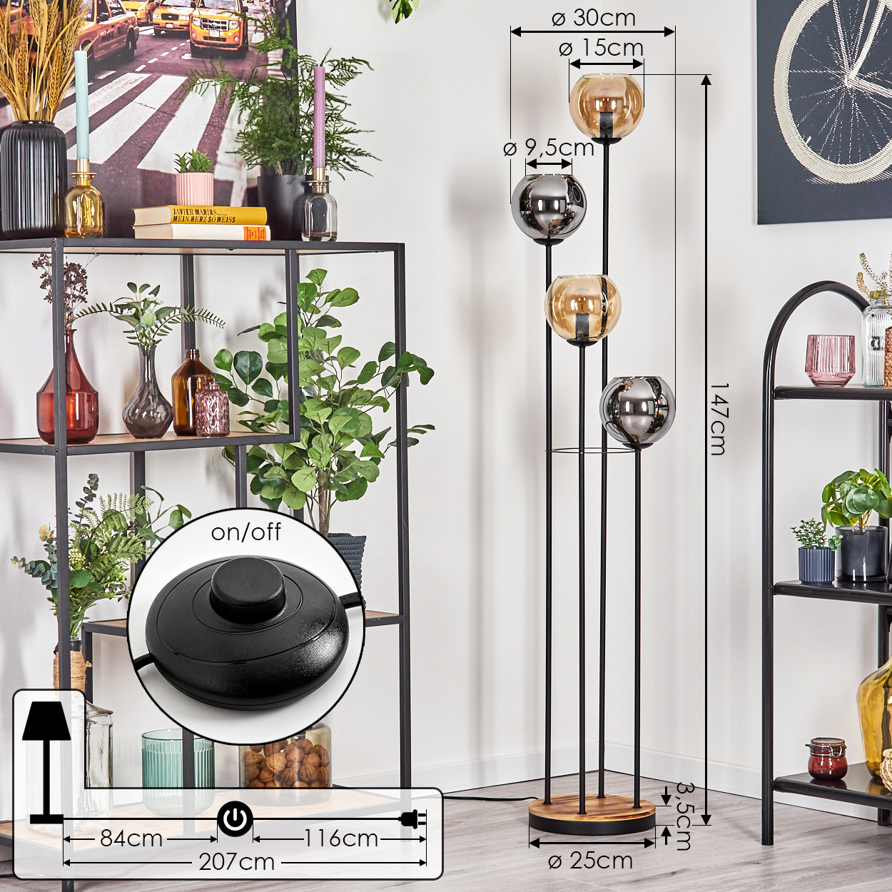 Eine hohe Stehlampe mit vier Glaskugeln, einem Holzsockel und einem Fußschalter. Regale mit Pflanzen und Dekorationen im Hintergrund.