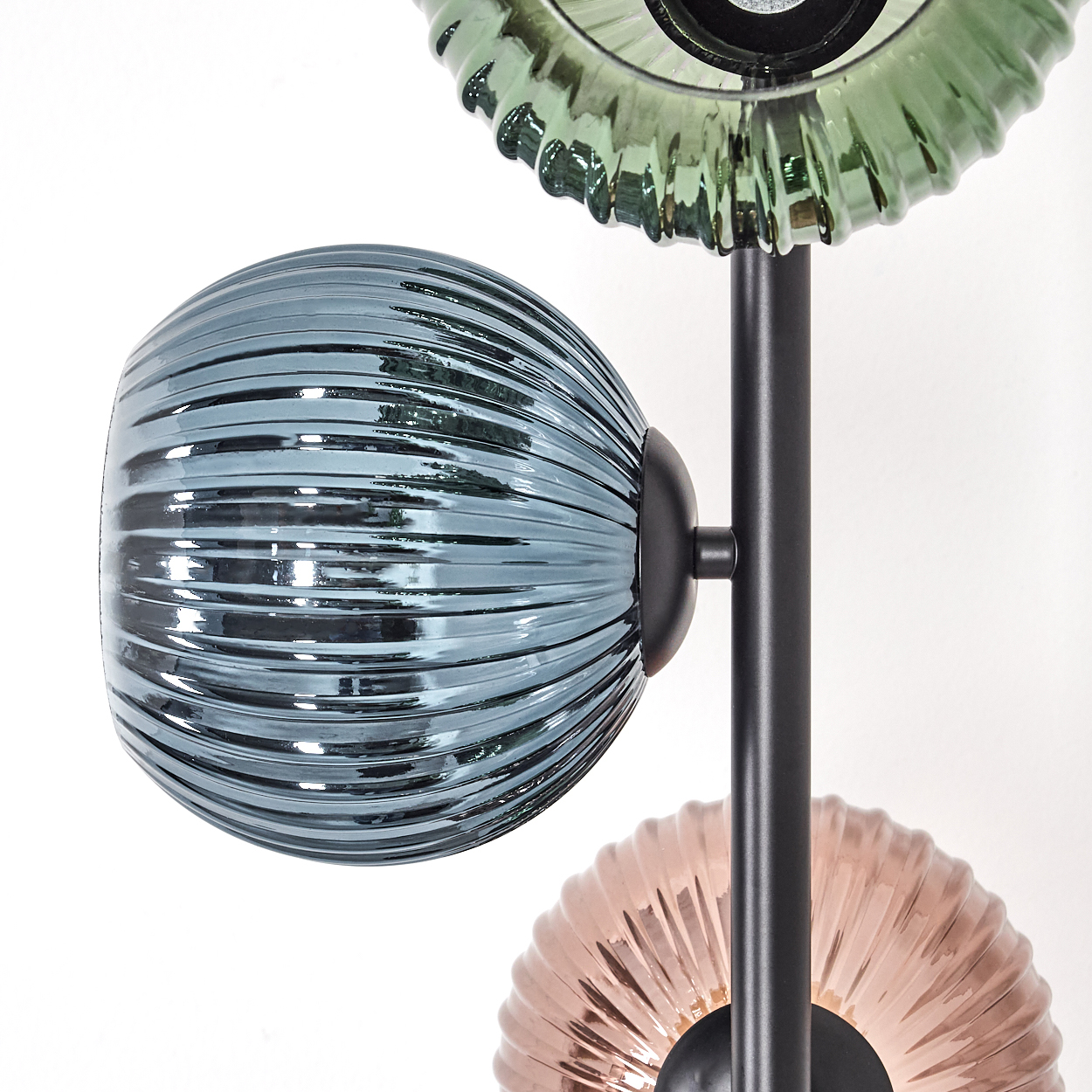 Nahaufnahme einer modernen Lampe mit drei Glasschirmen in Blau, Grün und Rosa. Schwarzer Metallstiel und weißer Hintergrund.