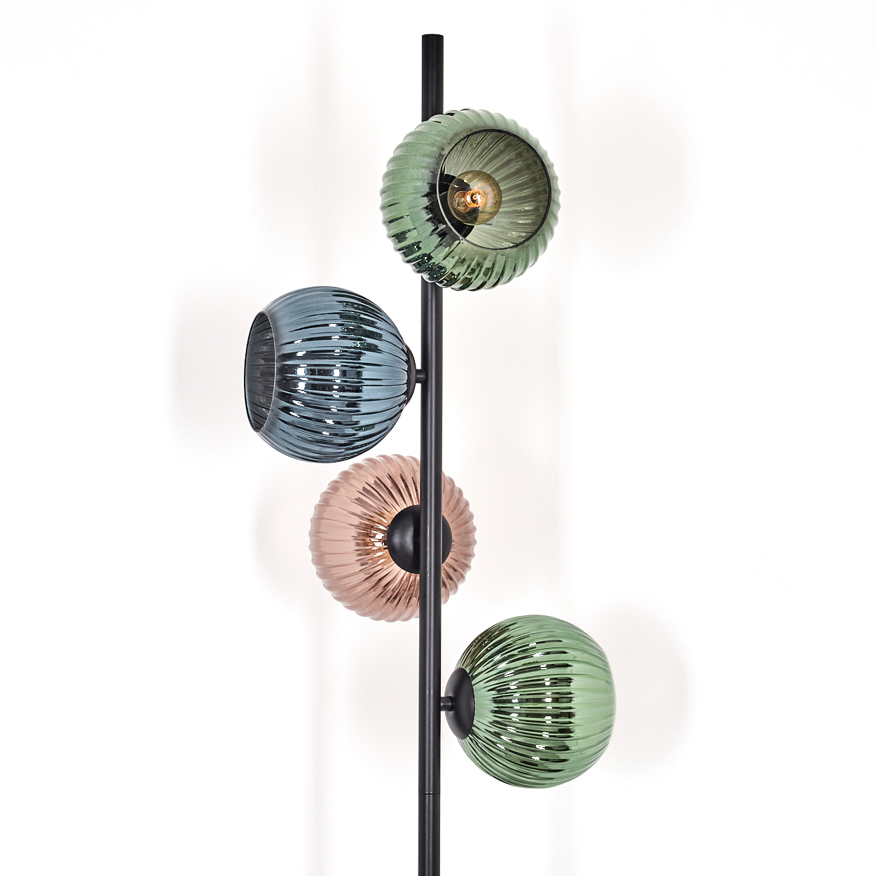Eine moderne Lampe mit vier gerippten Glasschirmen in Grün, Blau und Rosa. Sie steht vor einer weißen Wand.