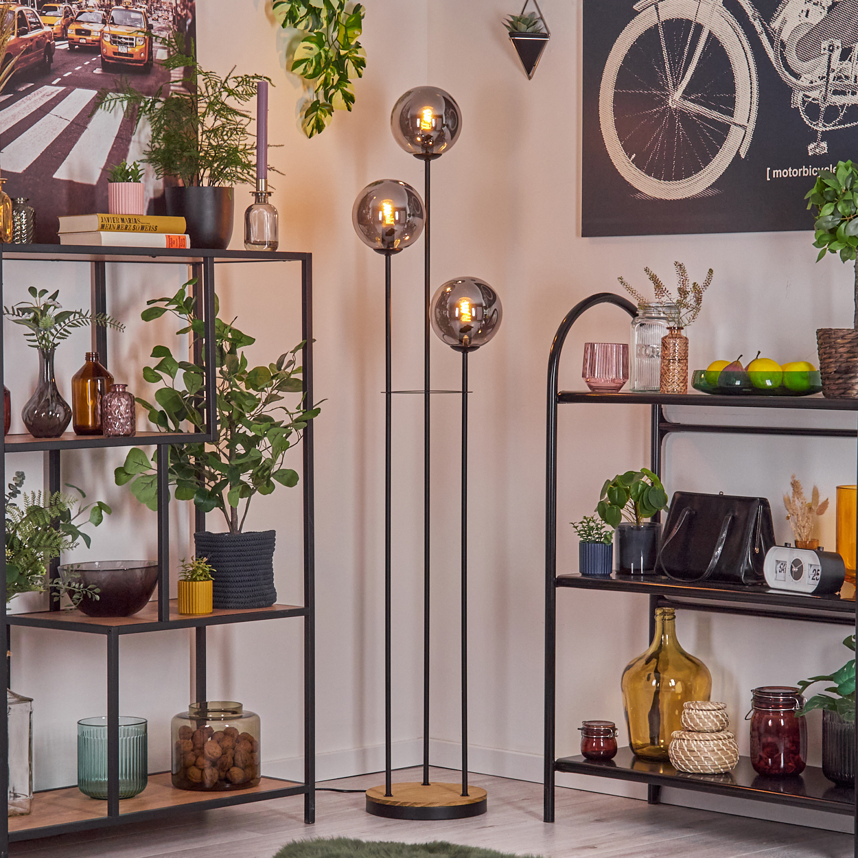 Wohnzimmer mit Regalen, Pflanzen und einer Dreifach-Lampe. Regale sind dekoriert. Ein Fahrrad-Kunstwerk an der Wand.