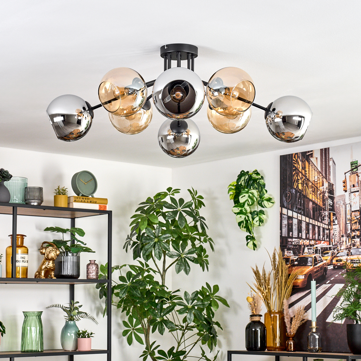 Eine moderne Deckenleuchte mit Glaskugeln. Regale mit Dekoration und Pflanzen im Vordergrund, Stadtbild im Hintergrund.