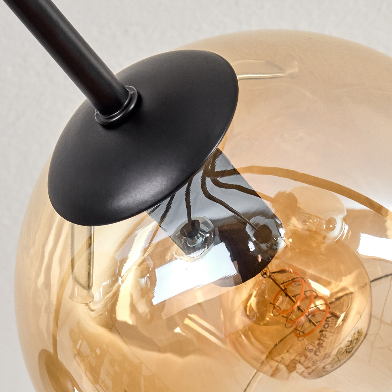 Nahaufnahme einer Lampe. Sie hat einen schwarzen Arm und einen runden, klaren, bernsteinfarbenen Glasschirm mit einer Glühbirne.
