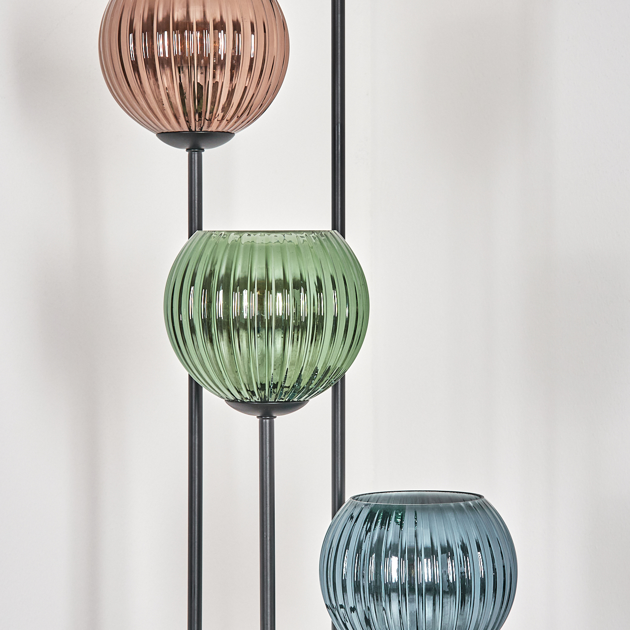 Drei kugelförmige Lampen in Kupfer, Grün und Blau, geripptes Glas, montiert auf einem schwarzen Metallrahmen, vor einer weißen Wand.