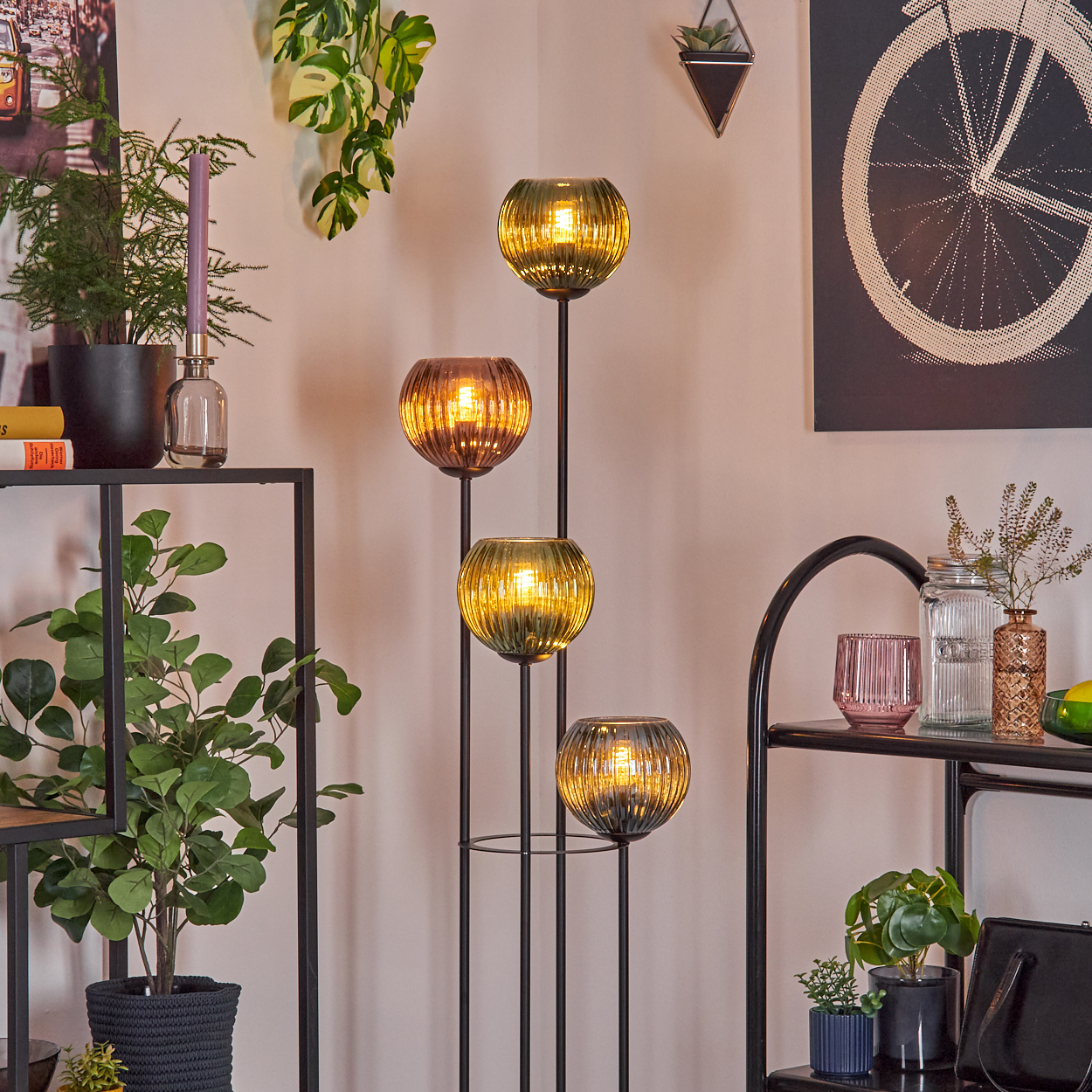 Eine dekorative Lampe mit vier Glaskugeln, Pflanzen und Regalen. Die Lampe strahlt warmes Licht aus. Pflanzen und andere Dekorationen sind sichtbar.