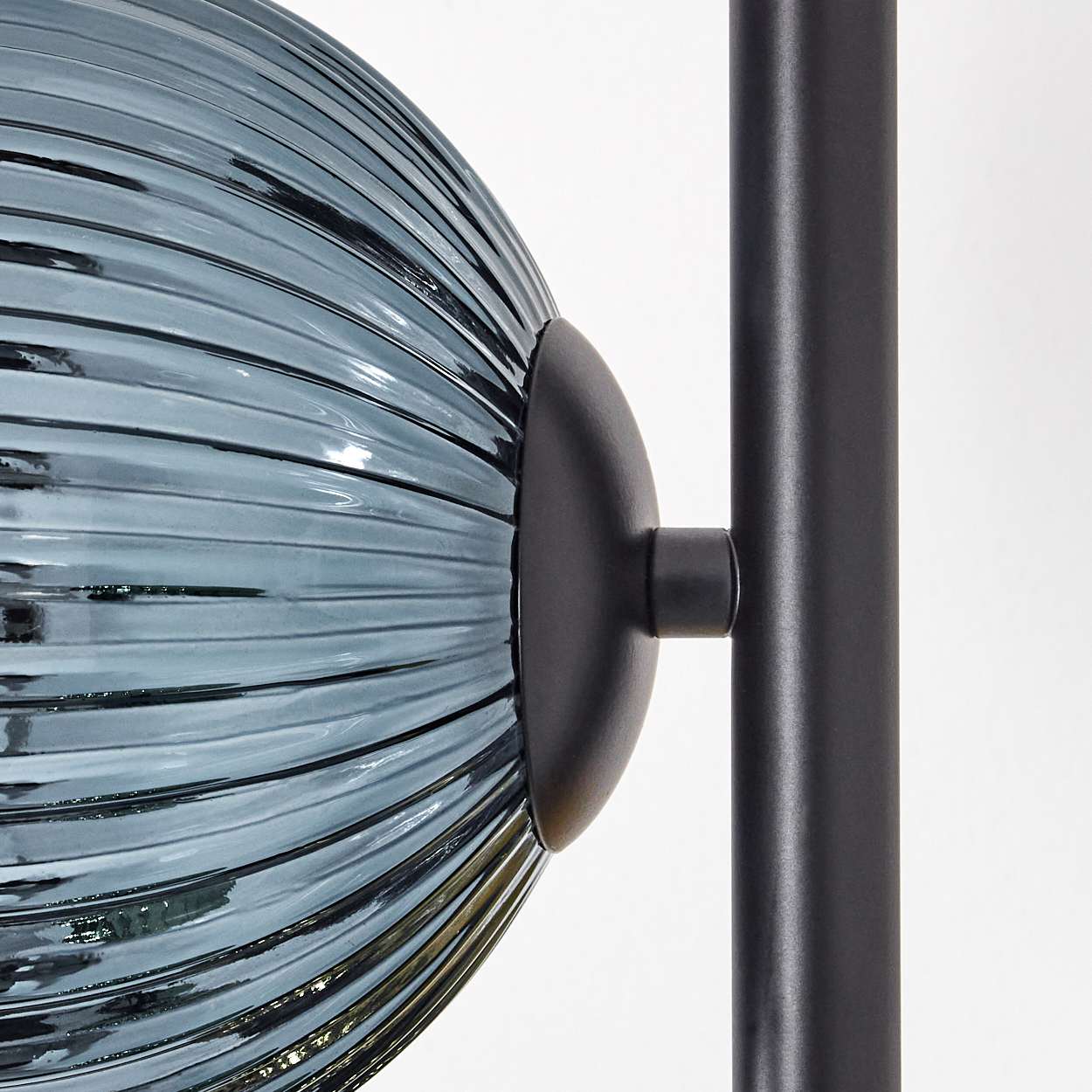 Nahaufnahme einer blauen, gerippten Glaskugel, die an einer schwarzen Metallstange befestigt ist. Weißer Hintergrund. Teile einer Lampe.