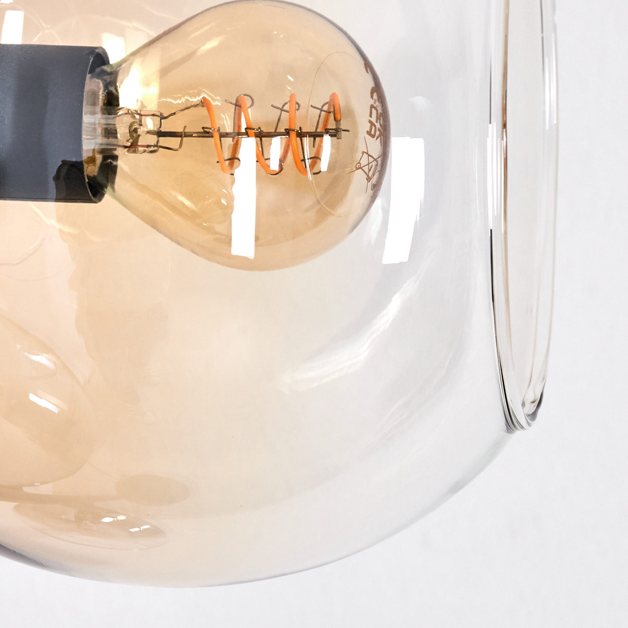 Nahaufnahme einer Glühbirne in einem Glaskörper. Die Glühbirne ist orange und hat einen Spiralglühfaden. Der Hintergrund ist weiß.