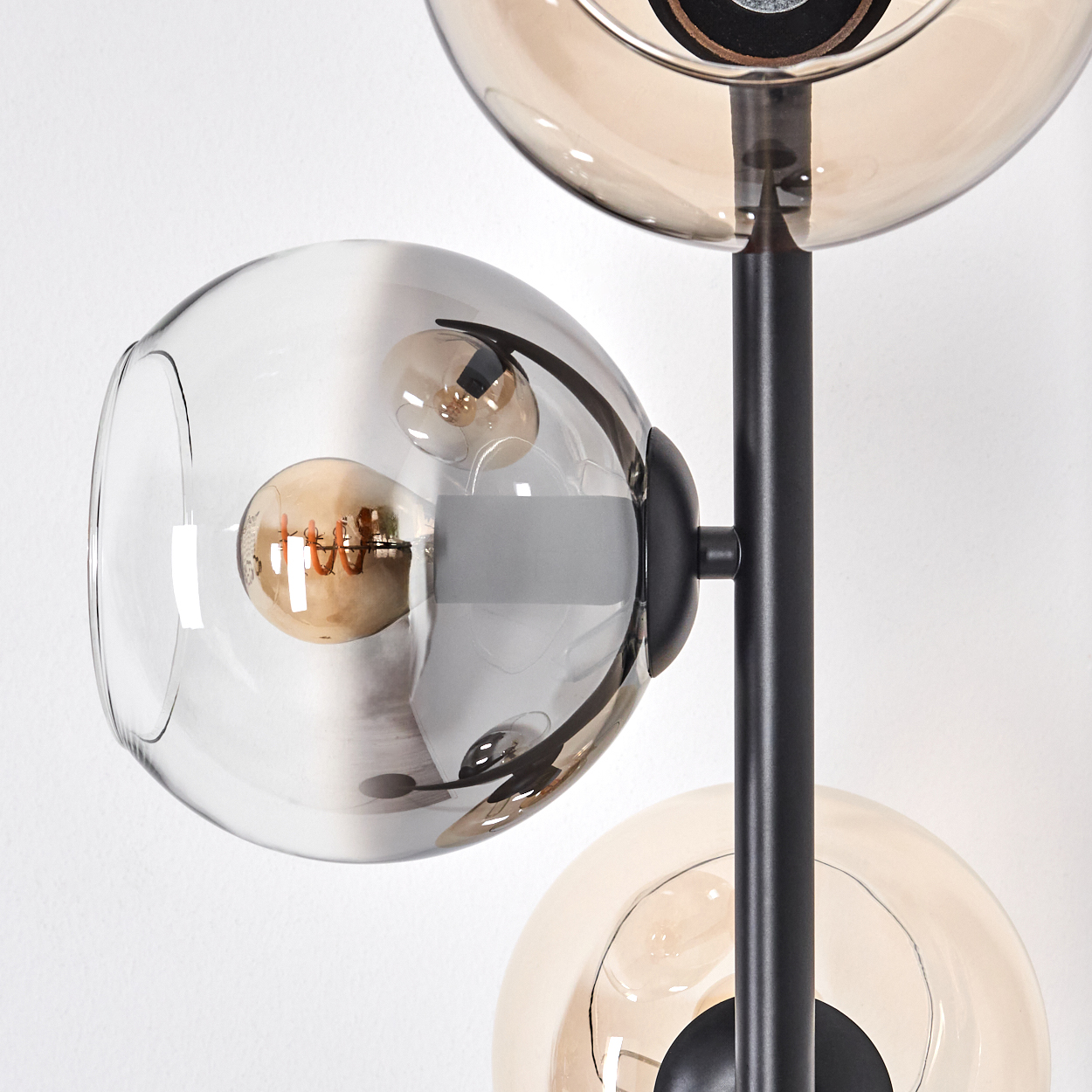 Nahaufnahme einer modernen Lampe mit drei Glaskugeln. Jede Kugel enthält eine Glühbirne. Die Halterung ist schwarz, vor weißem Hintergrund.