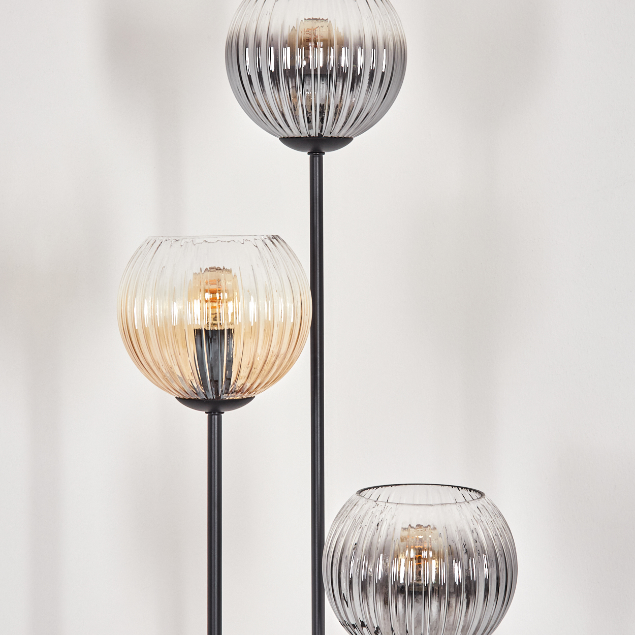 Eine moderne Stehlampe mit drei kugelförmigen Glasschirmen. Einer ist bernsteinfarben, zwei sind grau. Alle haben eine Glühbirne.
