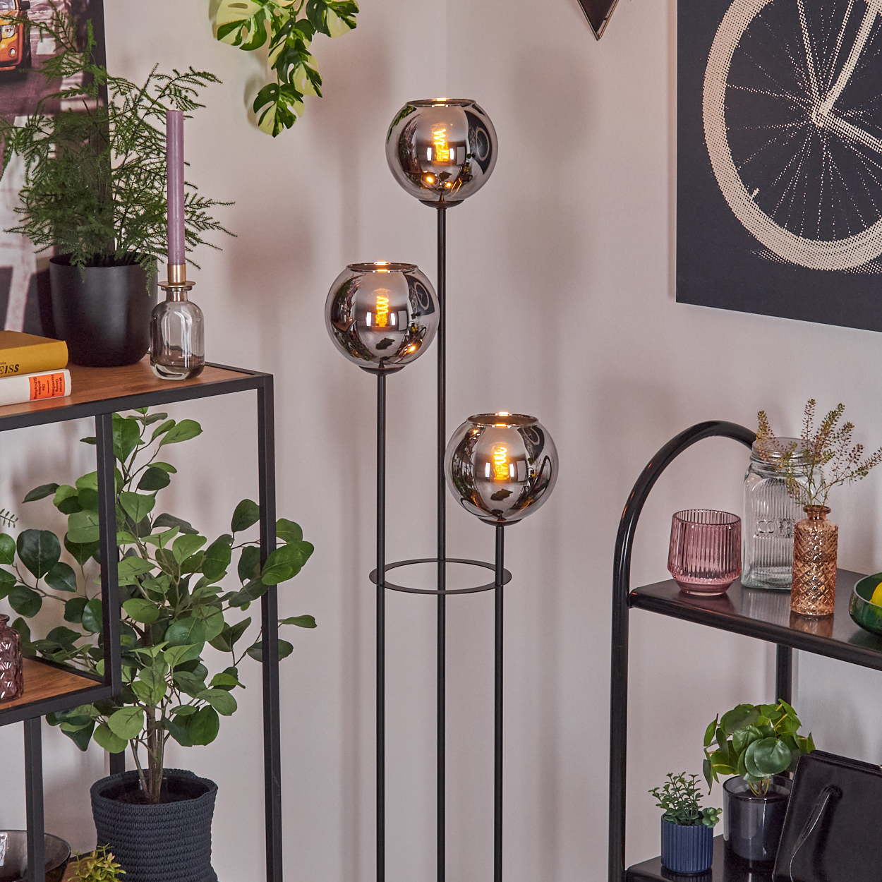 Ein Raum mit einer Stehlampe mit drei kugelförmigen Schirmen, Pflanzen und Regalen mit Dekorationsartikeln.