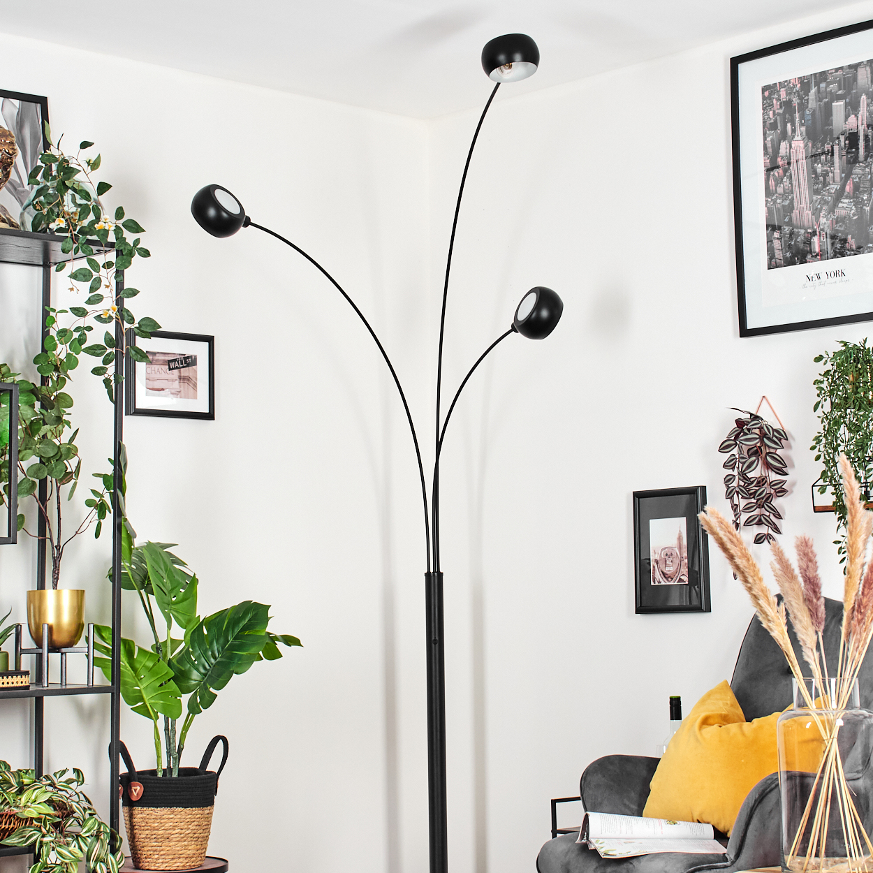 Ein modernes Wohnzimmer mit schwarzer Stehlampe, Pflanzen, grauem Sessel und gerahmten Bildern an der Wand.