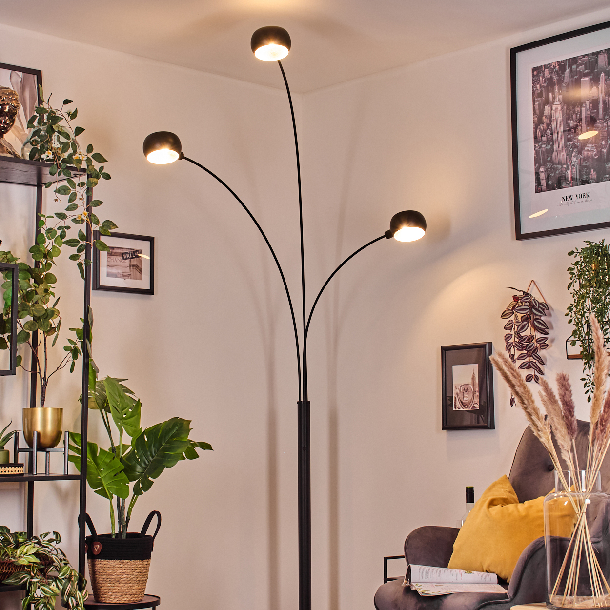 Ein modernes Wohnzimmer mit schwarzer Lampe, Pflanzen, gerahmtem Bild, grauem Sessel und gelbem Kissen.