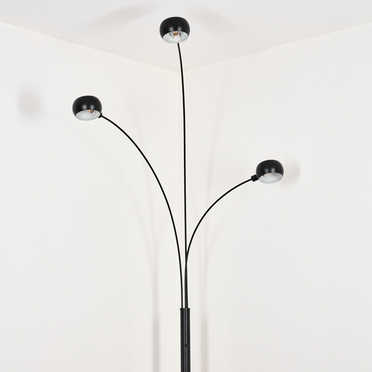 Eine schwarze Stehlampe mit drei verstellbaren Lichtern. Die Lampe steht in einer weißen Ecke. Jedes Licht hat ein silbernes Innere.