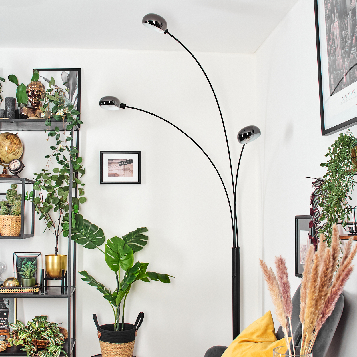 Ein modernes Wohnzimmer mit schwarzer Stehlampe, Pflanzen, einem grauen Stuhl und einem Bilderrahmen an der Wand. Die Wand ist weiß.