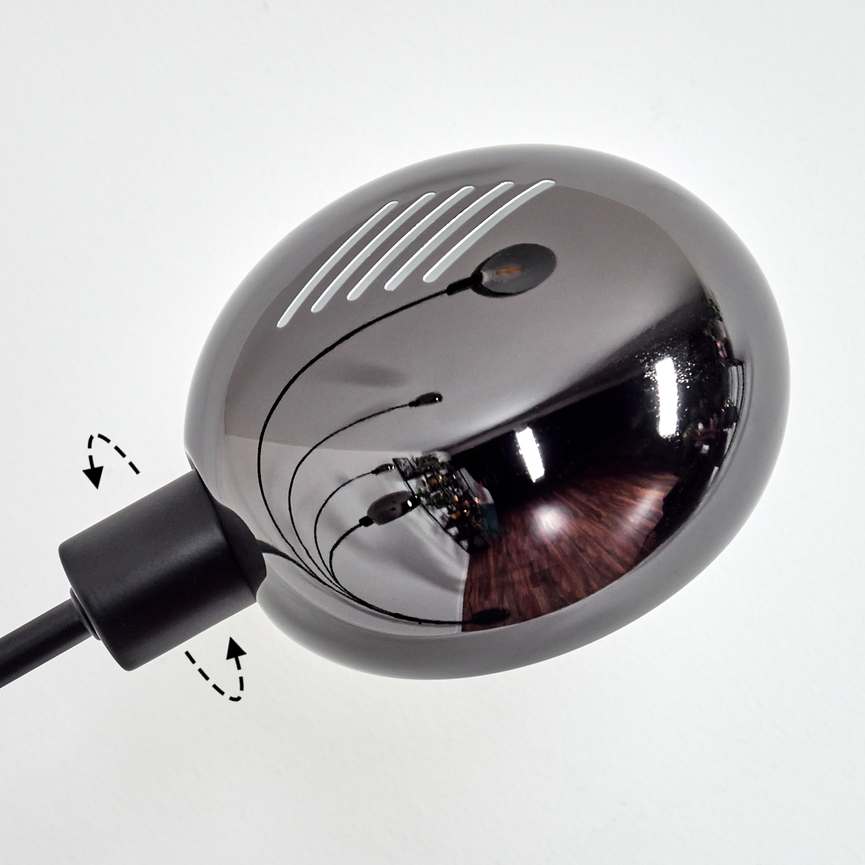Ein dunkler, reflektierender Lampenkopf mit einigen kleinen Lichtern. Er reflektiert einen Holzboden und andere Objekte. Die Lampe steht auf weißem Hintergrund.