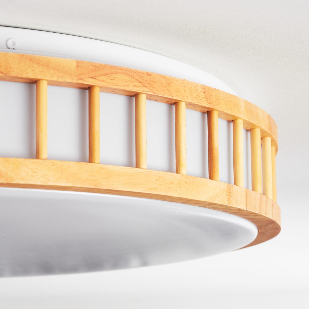 Nahaufnahme einer Deckenleuchte aus Holz und Weiß. Sie hat einen Holzrahmen mit vertikalen Lamellen, der ein weißes, rundes Licht umgibt.