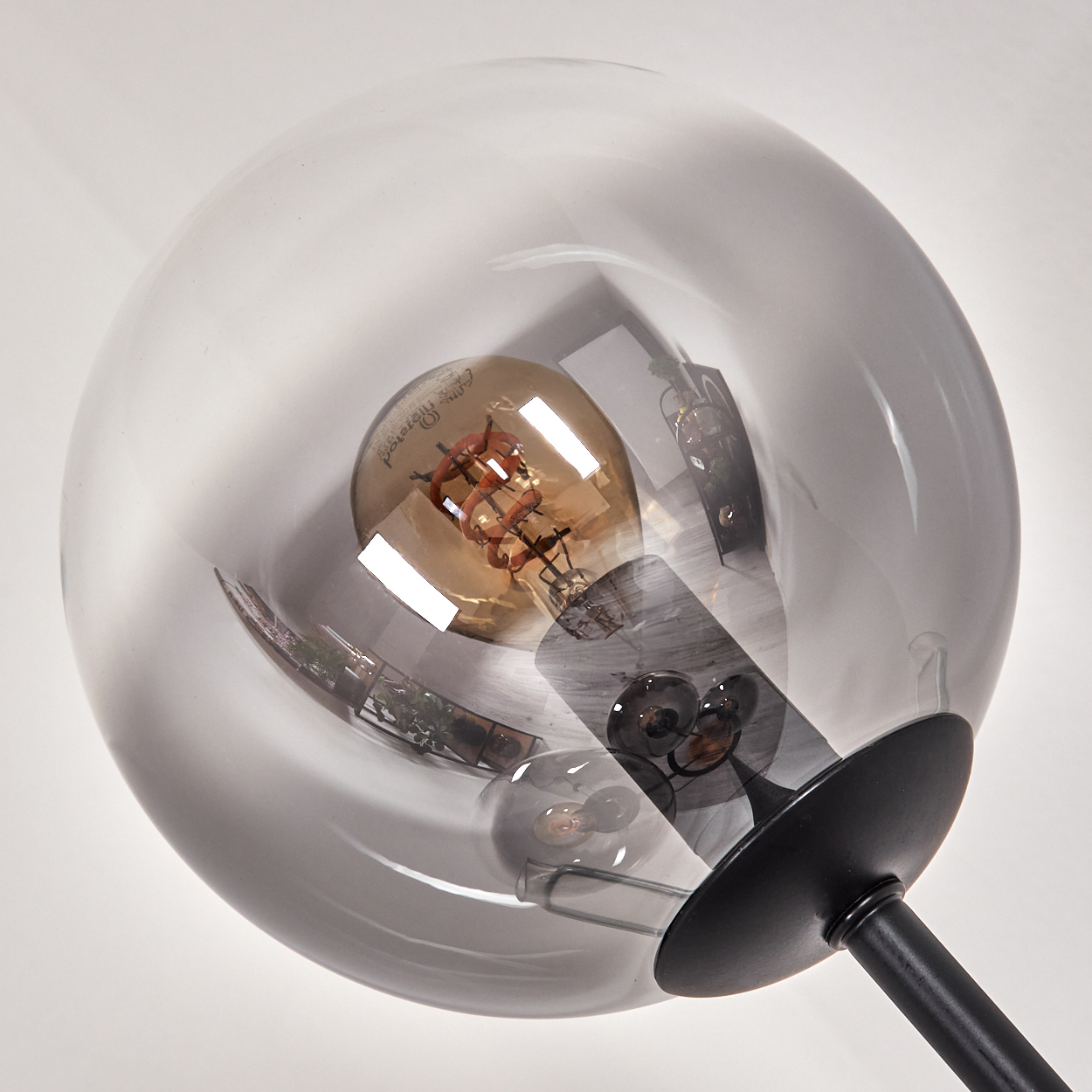 Nahaufnahme einer modernen Lampe. Sie hat einen transparenten, kugelförmigen Schirm mit einer sichtbaren Glühbirne und einen schwarzen Sockel.