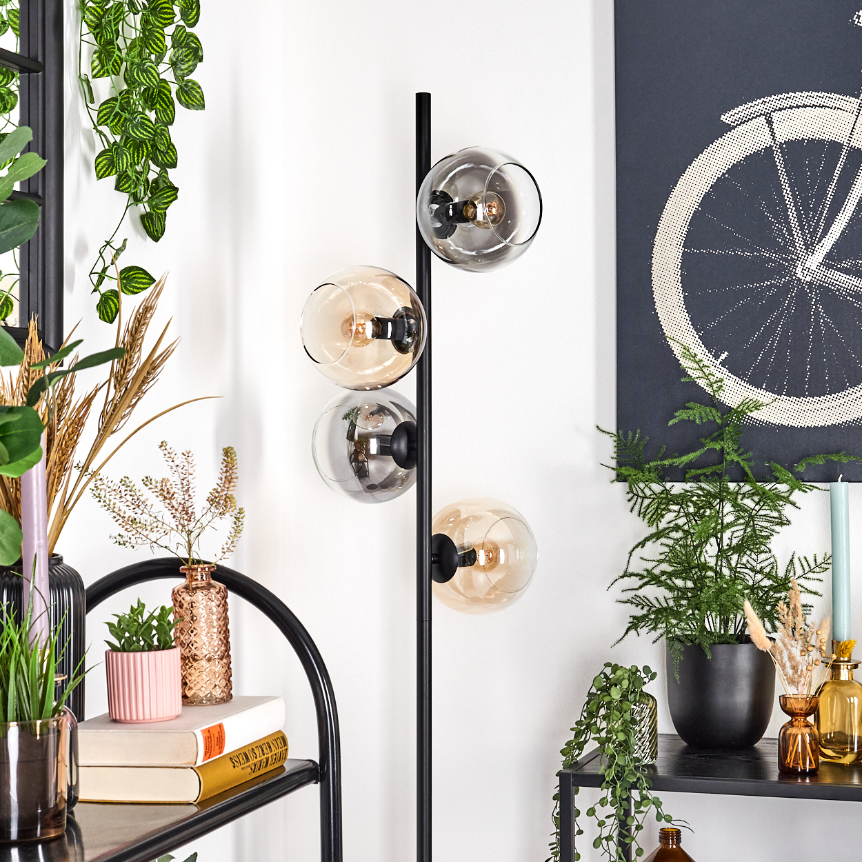 Eine moderne Lampe mit vier Kugellampen. Der Hintergrund umfasst Pflanzen, ein schwarzes Regal und ein Bild eines Fahrradrads.