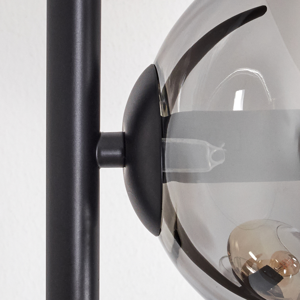 Nahaufnahme einer schwarzen Metall-Lampenstange mit einem kugelförmigen Glasschirm. Im Schirm ist eine Glühbirne zu sehen. Weißer Hintergrund.