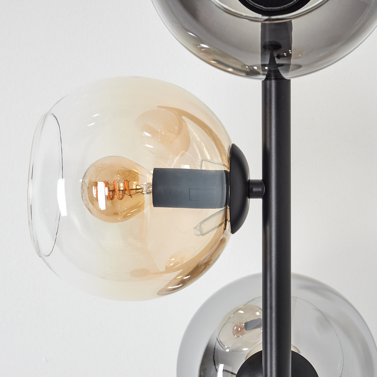 Eine moderne Lampe mit drei kugelförmigen Schirmen. Der mittlere Schirm hat eine sichtbare Glühbirne. Die Lampe hat ein schwarzes Metallgestell.