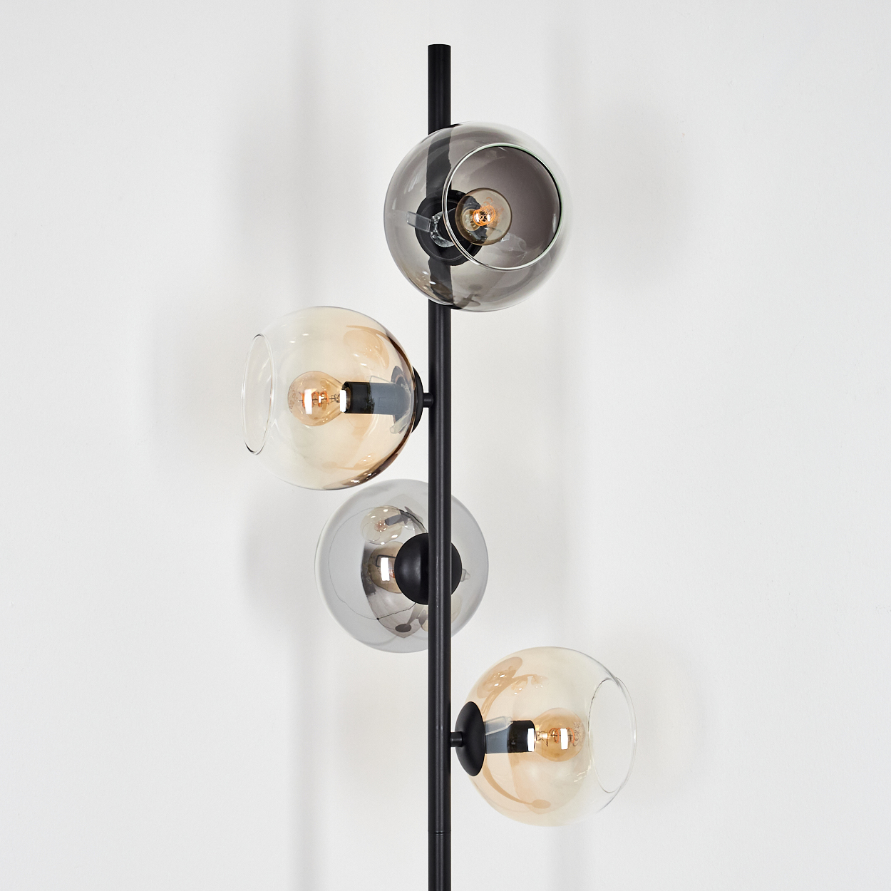 Eine moderne Stehlampe mit vier Glasschirmen in verschiedenen Farben, jeweils mit einer Glühbirne. Sie steht vor einer weißen Wand.