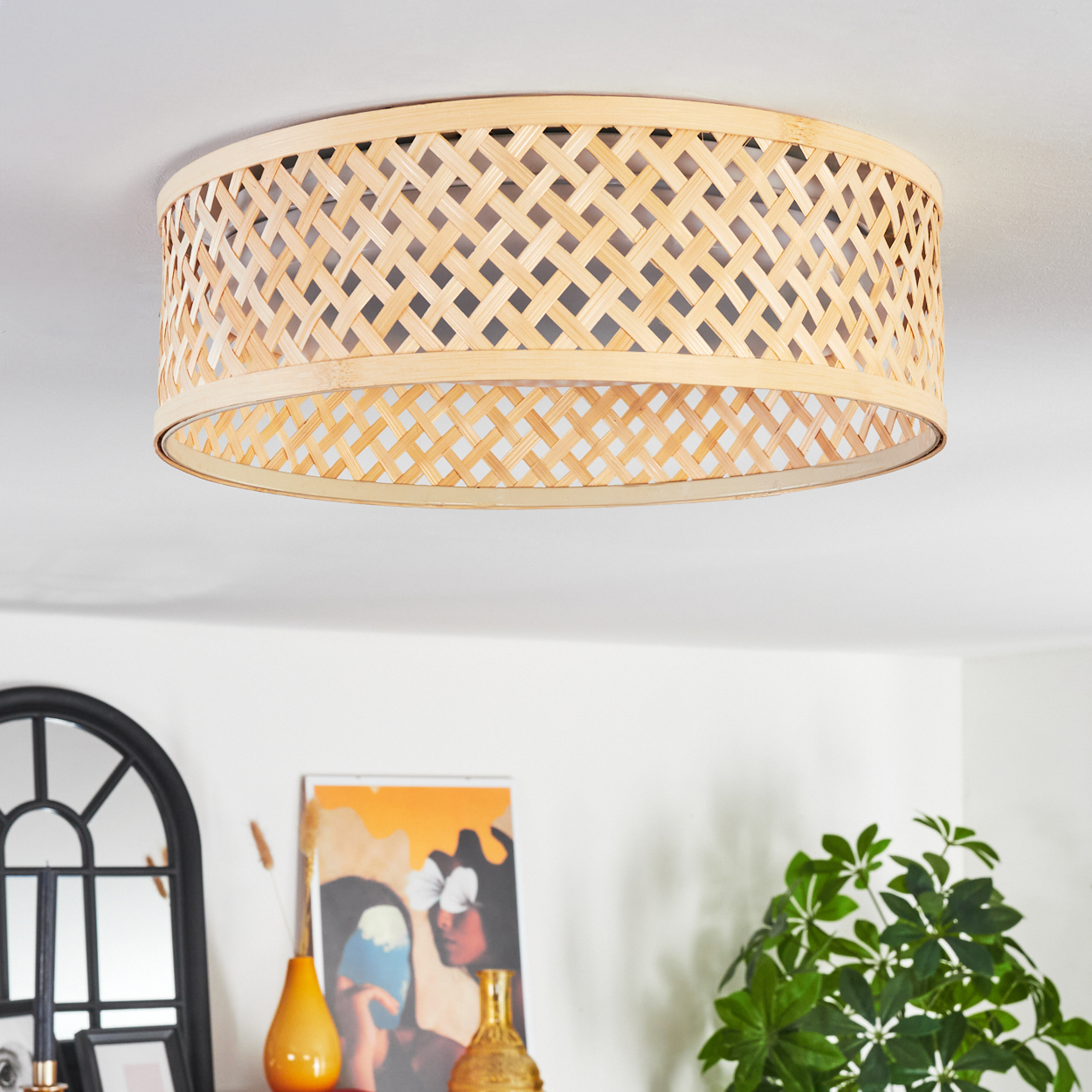 Eine Deckenlampe aus gewebtem Bambus. Darunter sind ein Spiegel, Kunstwerke, Vasen und eine grüne Pflanze zu sehen.