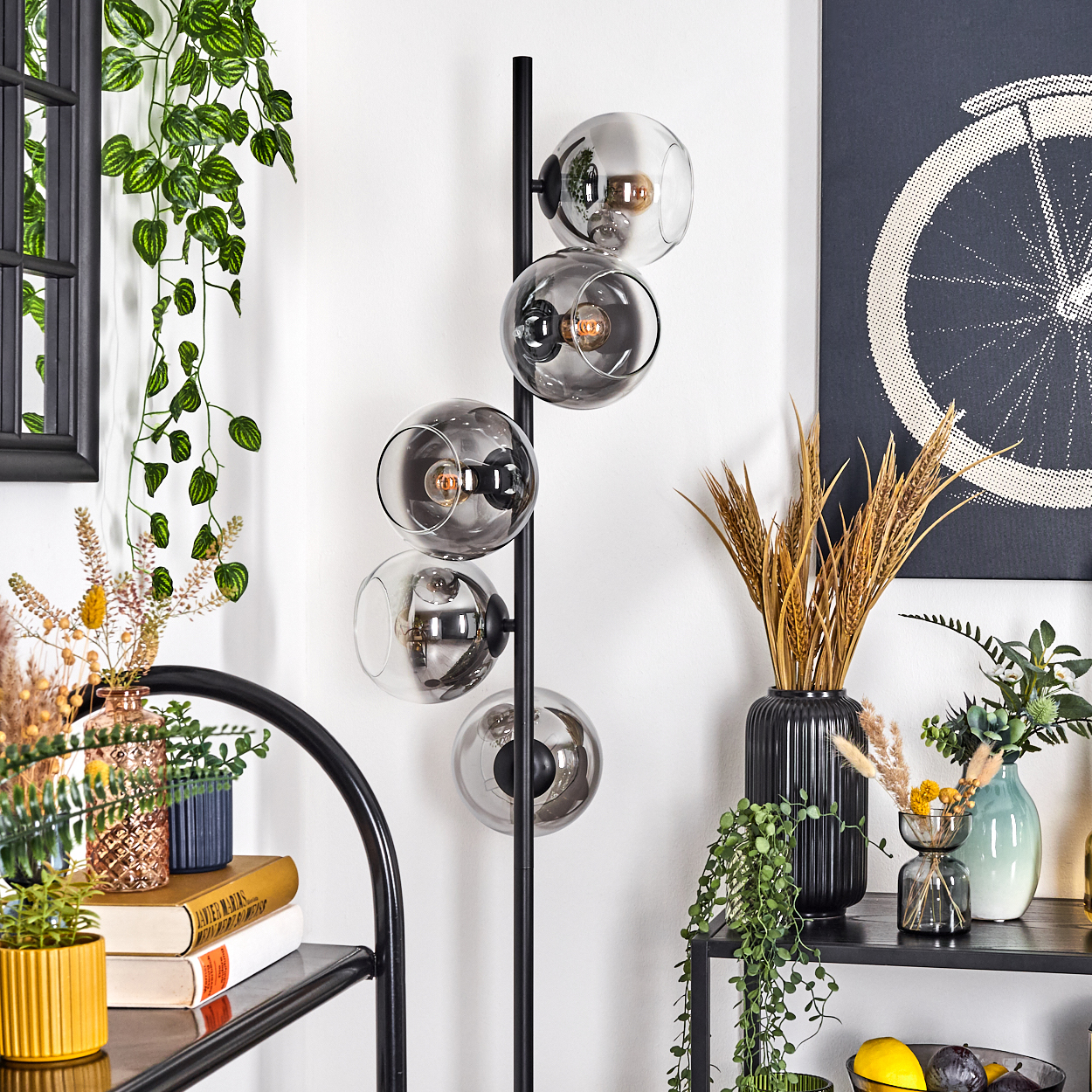 Ein modernes Wohnzimmer mit Stehlampe, Pflanzen, schwarzem Regal und Fahrradrad-Kunstwerk.