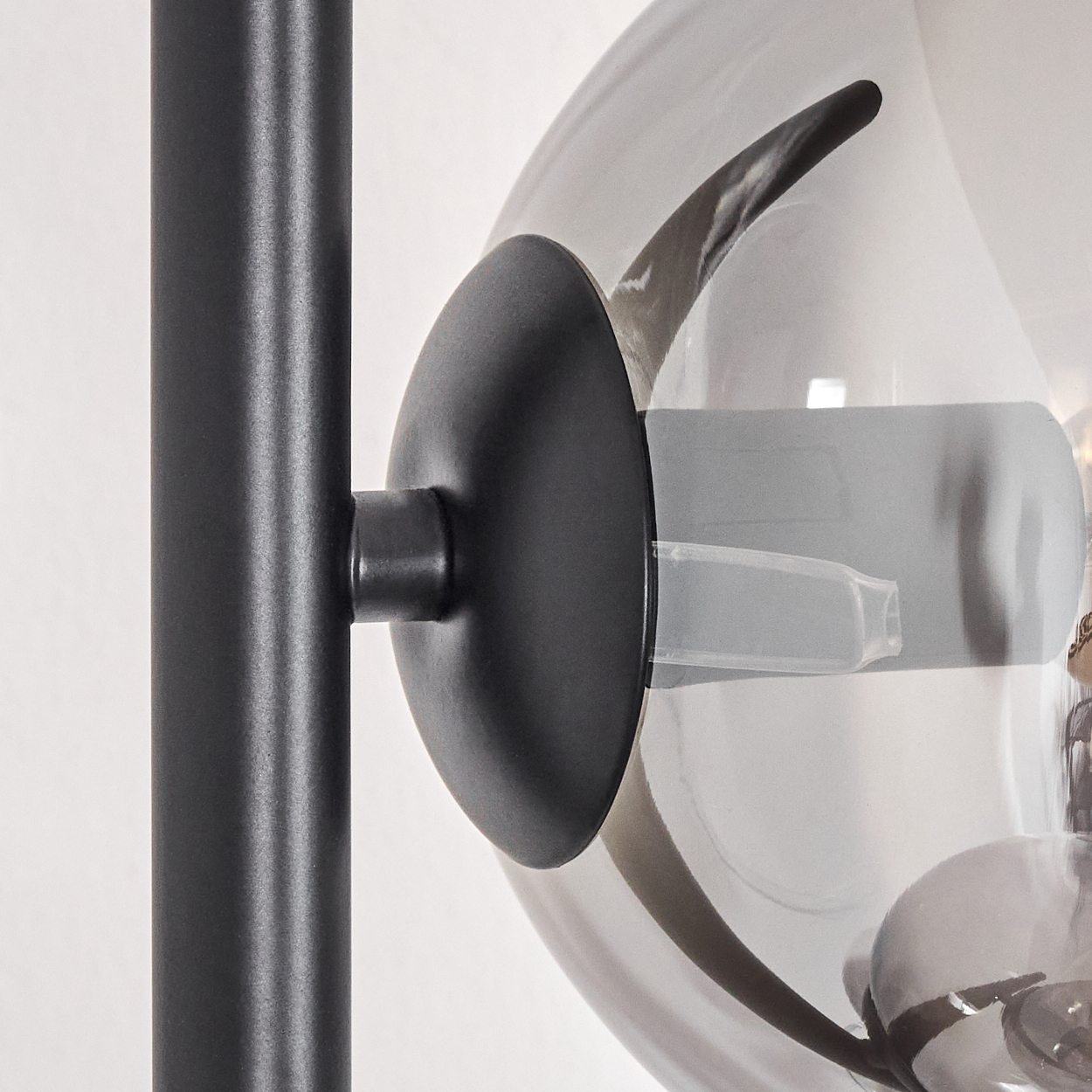 Nahaufnahme einer schwarzen Lampe mit rundem, rauchigem Glasschirm. Eine schwarze Metallstange verbindet sich mit dem Schirm.