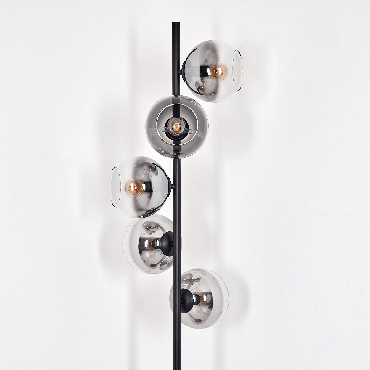 Eine moderne Lampe mit fünf Glaskugeln, jede mit einer Glühbirne. Die Lampe ist schwarz und steht vor einer weißen Wand.