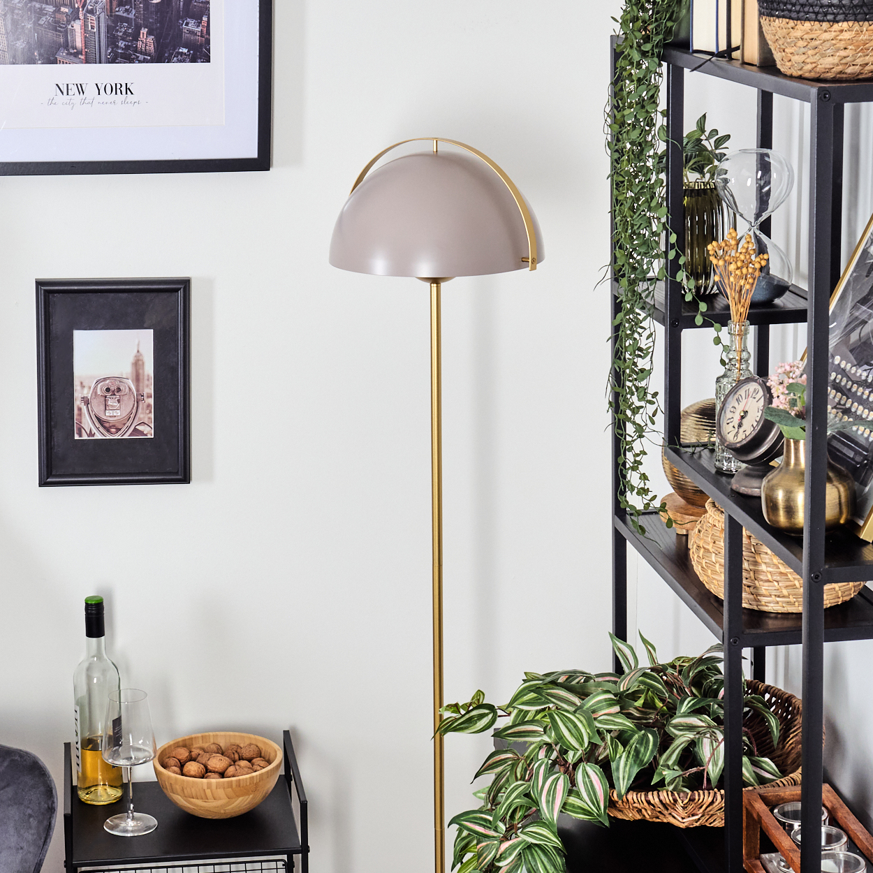 Ein Raum mit einer Stehlampe, einem Regal mit Dekorationen und einem kleinen Tisch mit einer Schüssel Nüsse und einer Weinflasche.