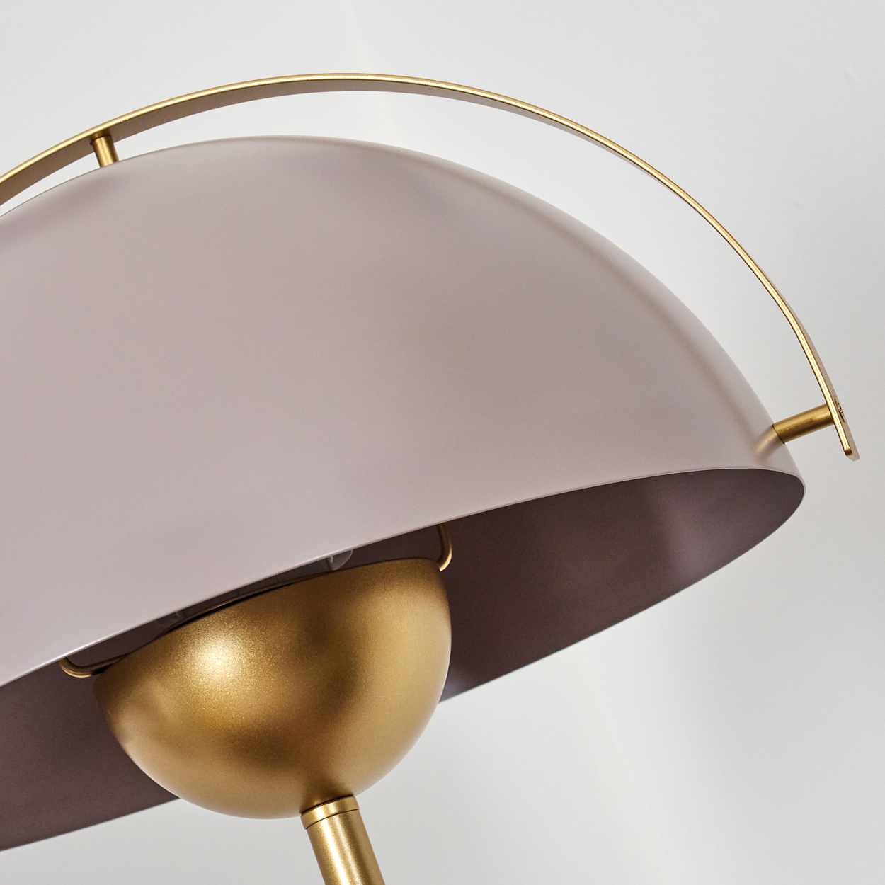 Nahaufnahme einer modernen Lampe. Sie hat einen goldenen Sockel und einen grauen, kuppelförmigen Schirm mit einem goldenen Bogen. Der Hintergrund ist weiß.