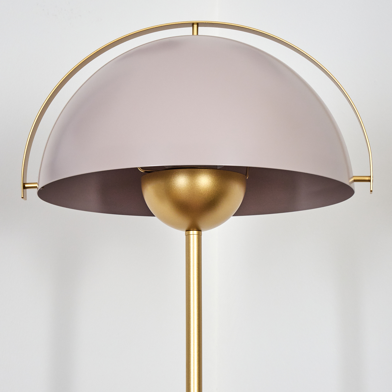 Eine moderne Lampe mit goldenem Stiel und Akzenten. Der Lampenschirm ist helllila und die Unterseite braun. Ein goldener Halbkreis umgibt ihn.