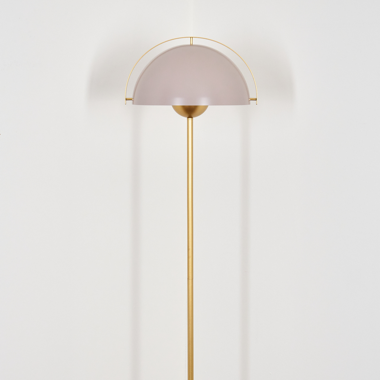 Eine moderne Stehlampe mit goldenem Stiel, halbkugelförmigem Schirm und gebogener Halterung. Der Hintergrund ist eine weiße Wand.