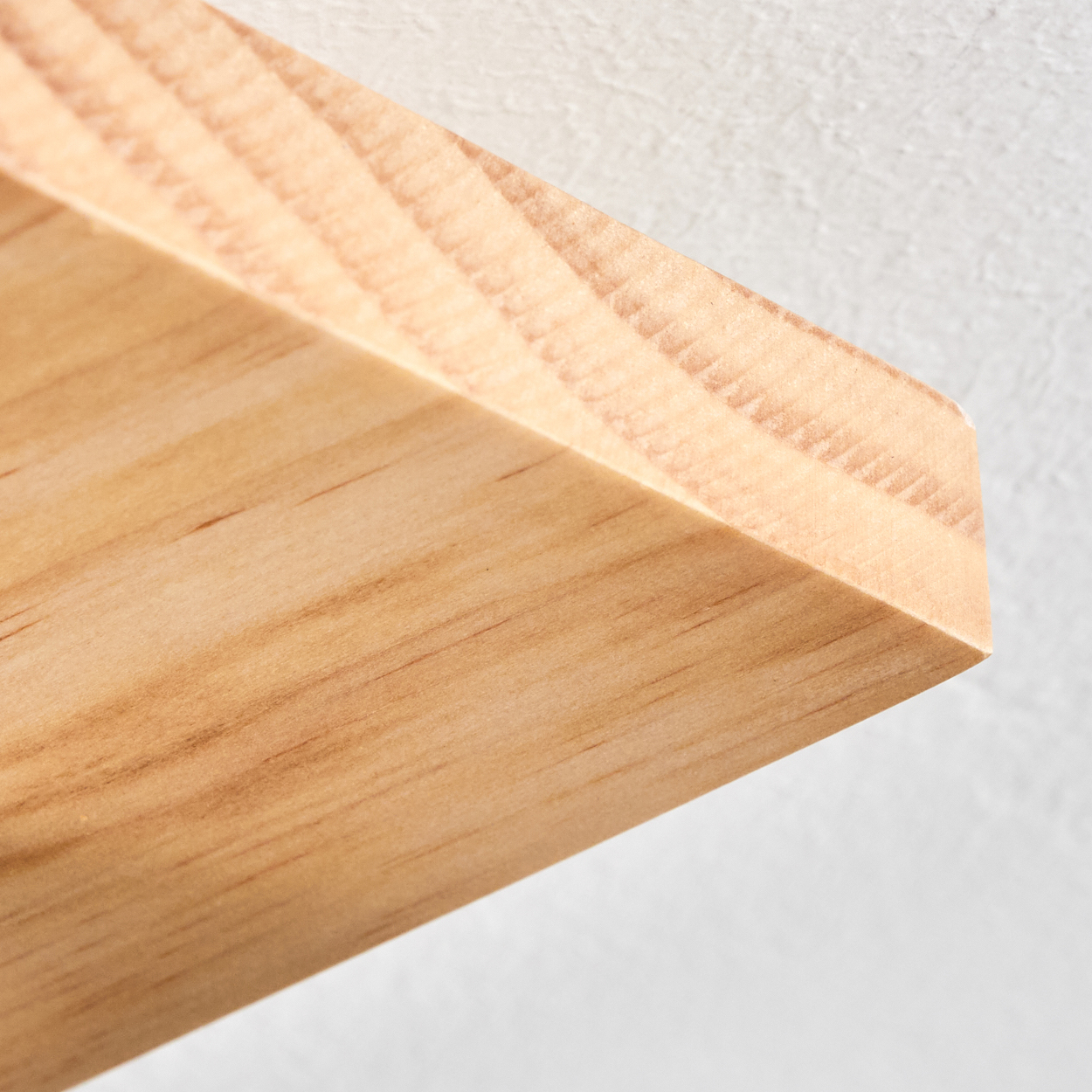 Nahaufnahme einer Holzeckkante vor weißer Wand. Die Holzmaserung ist sichtbar. Das Regal ist hellbraun.