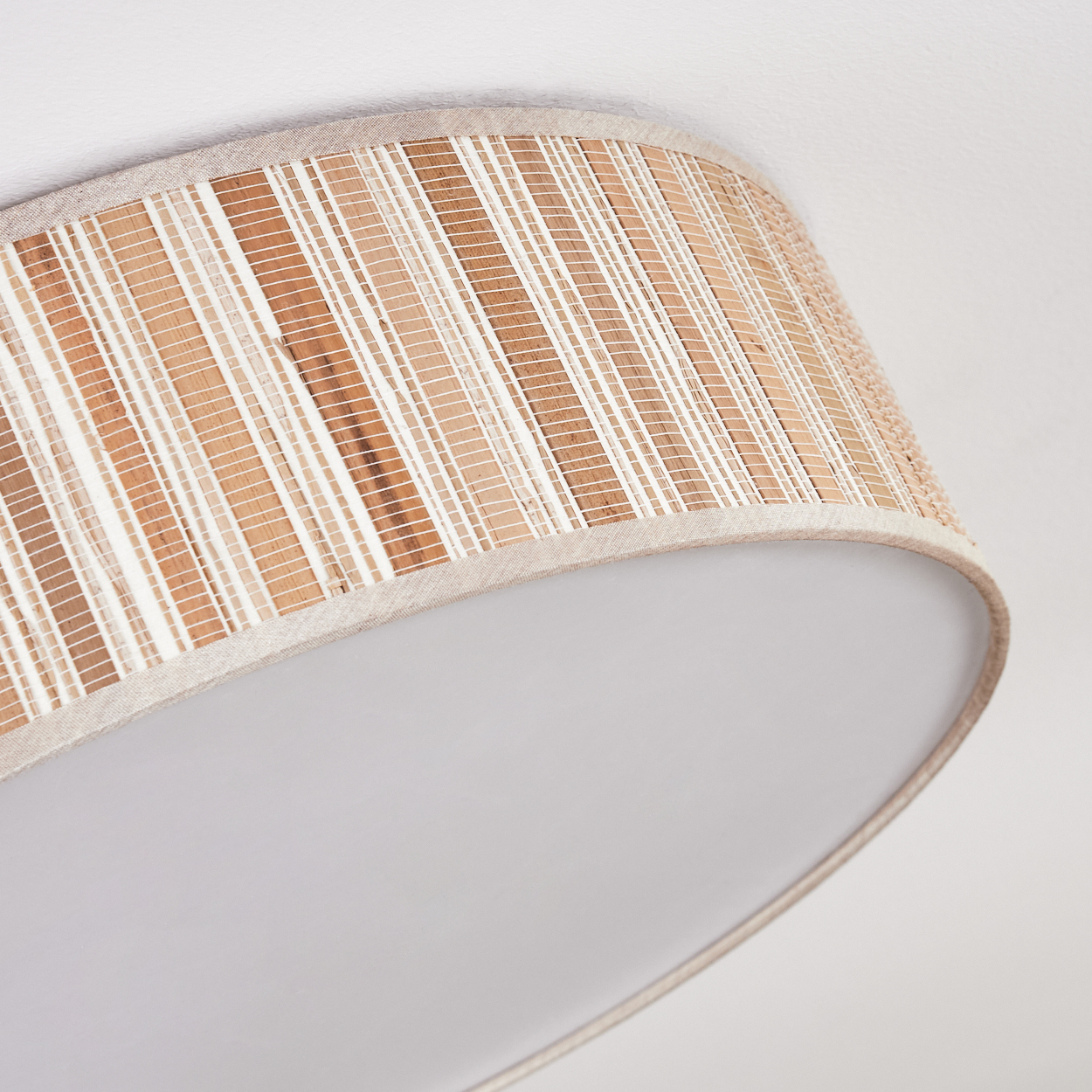 Nahaufnahme eines Lampenschirms. Der Lampenschirm hat ein gewebtes Muster mit beige-weißen Streifen. Der Boden ist weiß.