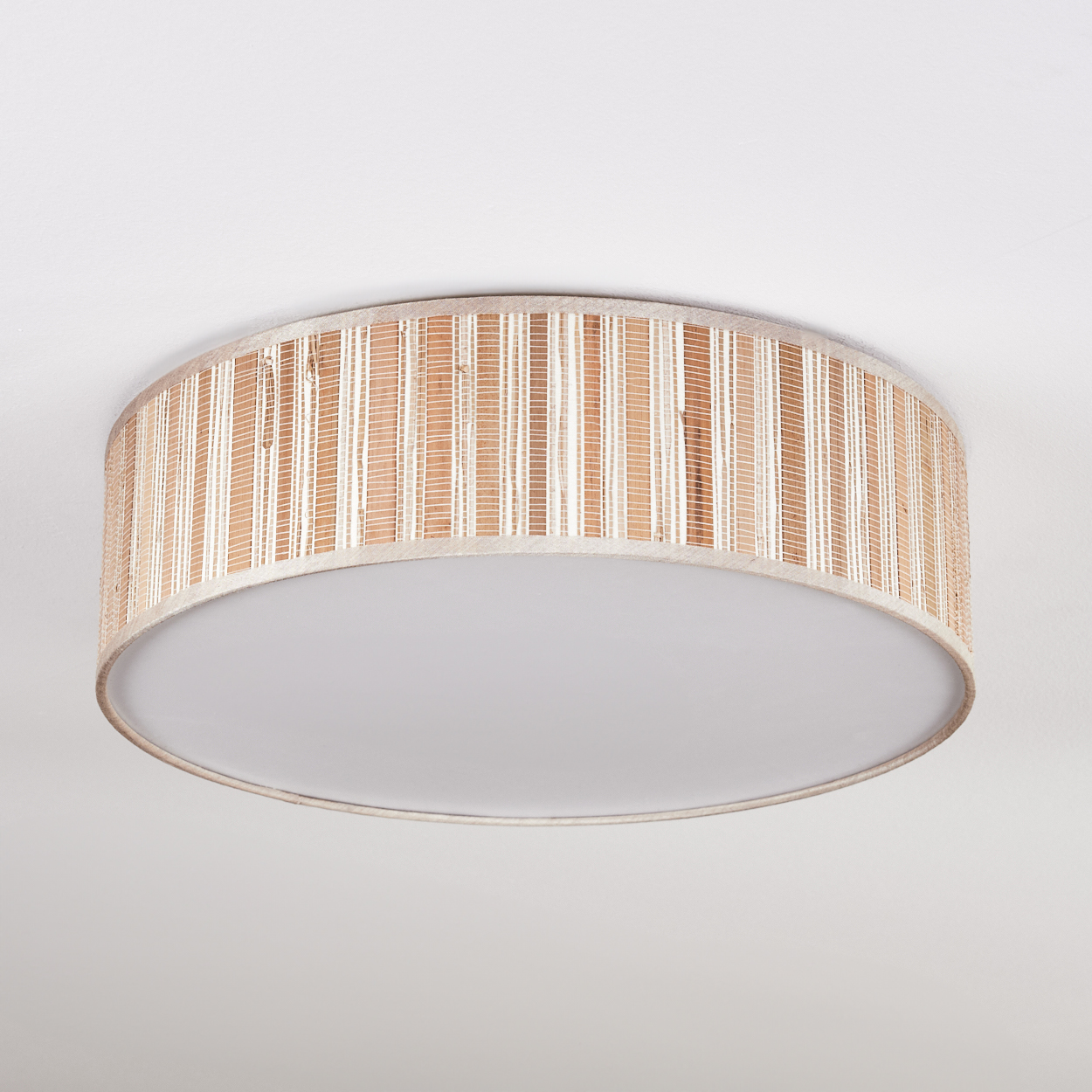 Eine runde Deckenlampe mit einem gewebten, hellbraunen Schirm und einem weißen, flachen Boden. Der Hintergrund ist schlicht weiß.