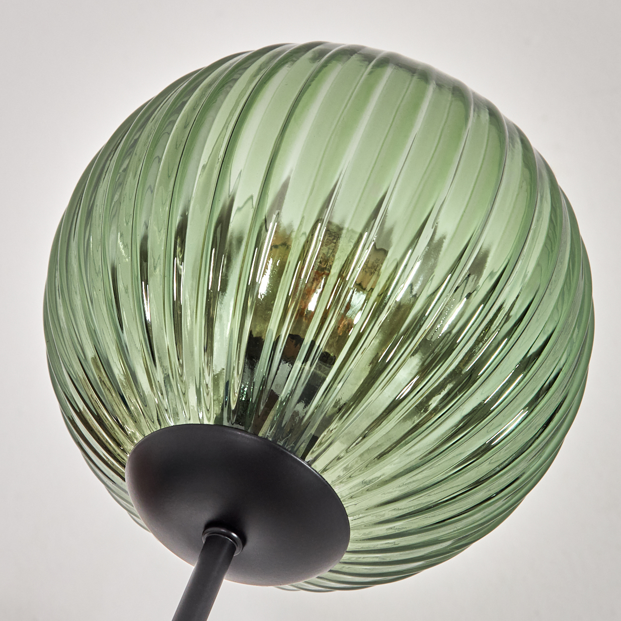 Ein grüner, geriffelter Glasschirm. Darunter ein schwarzer kreisförmiger Sockel und Stiel vor weißem Hintergrund.