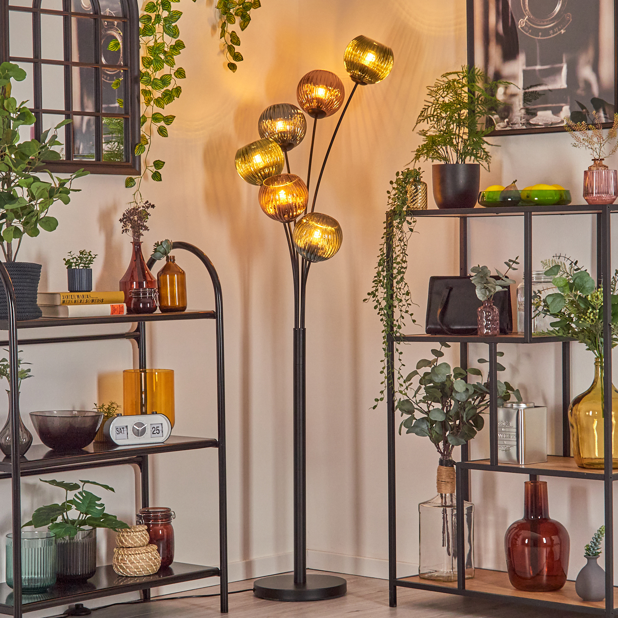 Ein modernes Wohnzimmer mit einer schwarzen Stehlampe mit Glaskugeln, Regalen mit Pflanzen und Dekorationen.