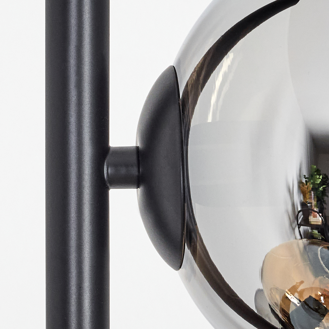 Nahaufnahme einer schwarzen Lampe. Sie hat einen runden, reflektierenden Glasschirm. Die Lampe steht vor weißem Hintergrund.