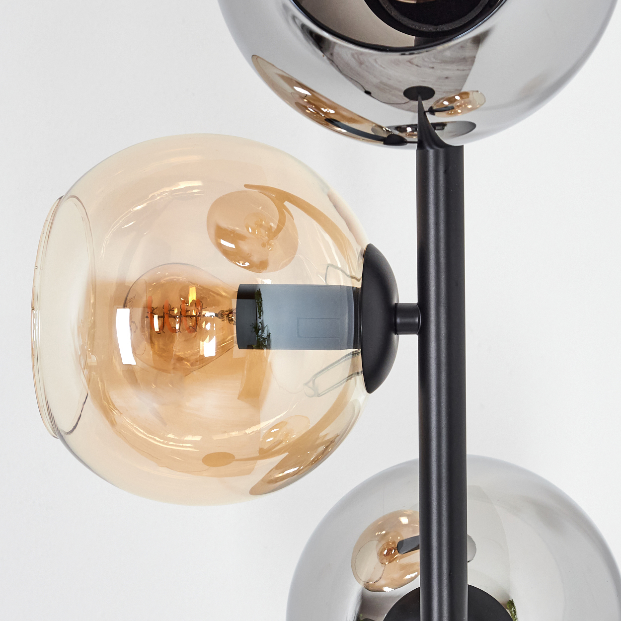 Moderne Lampe mit drei kugelförmigen Schirmen. Einer ist bernsteinfarben, zwei sind verspiegelt. Eine schwarze Stange trägt die Schirme.
